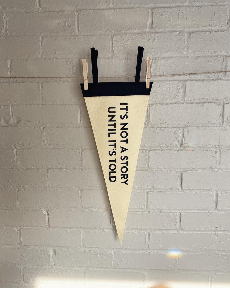 A custom pennant in cream and black felt and the phrase "It's not a story until it's told" printed in black ink