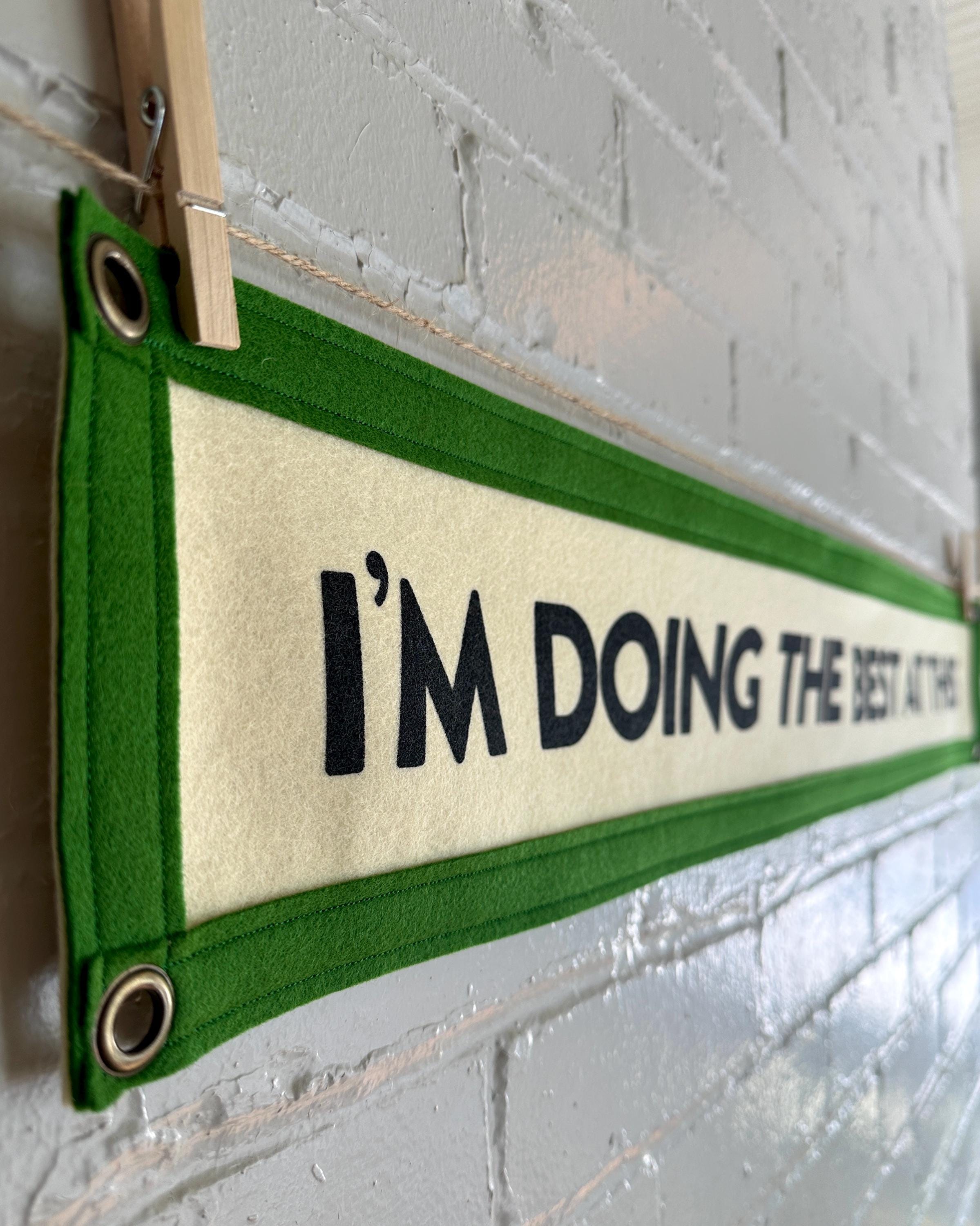 Close up side view of a cream banner with green trim and black lettering that reads "I'm doing the best at this"