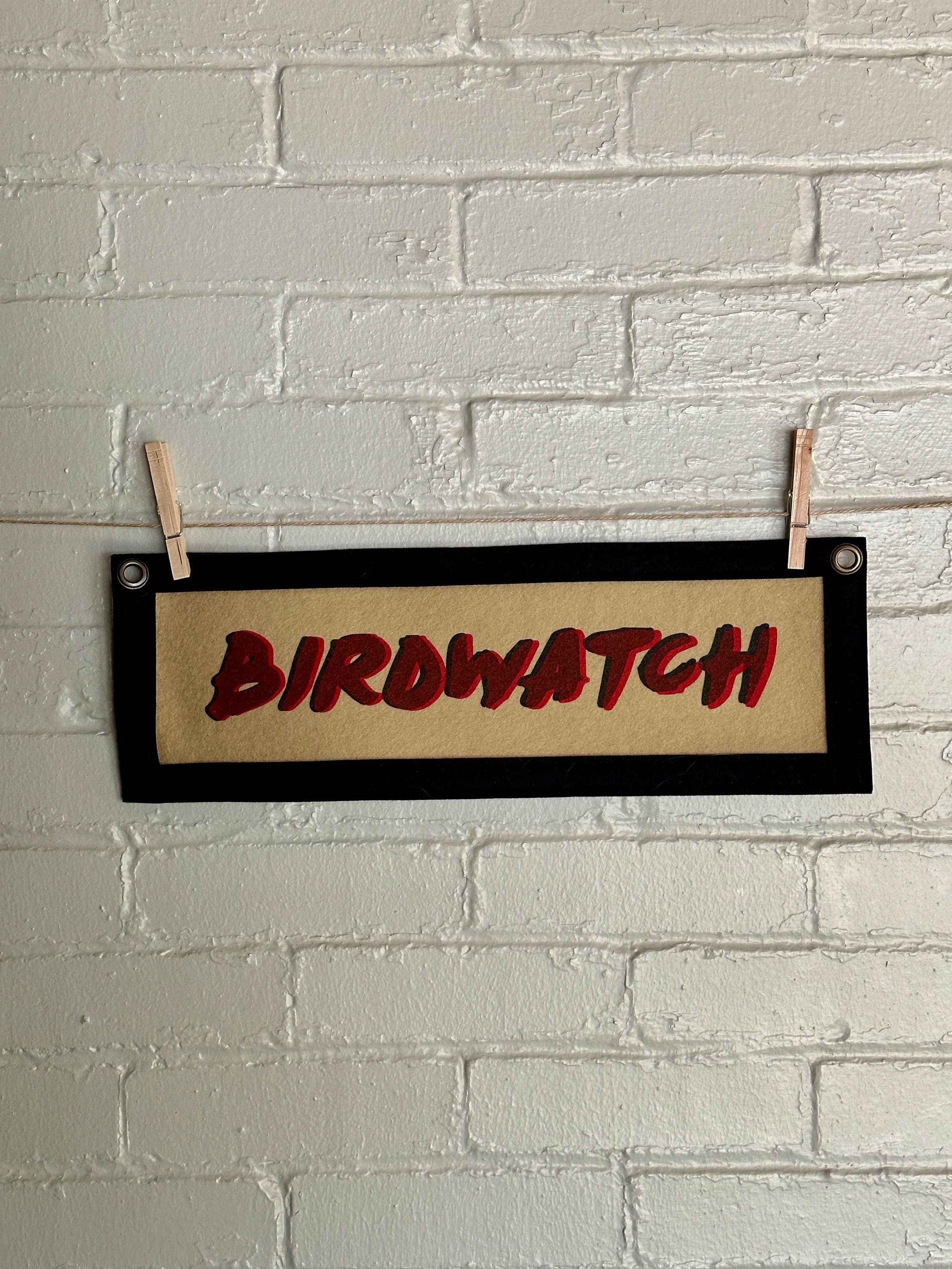 Light brown banner with black trim and double printed red and black lettering reading "BIRDWATCH"