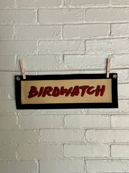 Light brown banner with black trim and double printed red and black lettering reading "BIRDWATCH"