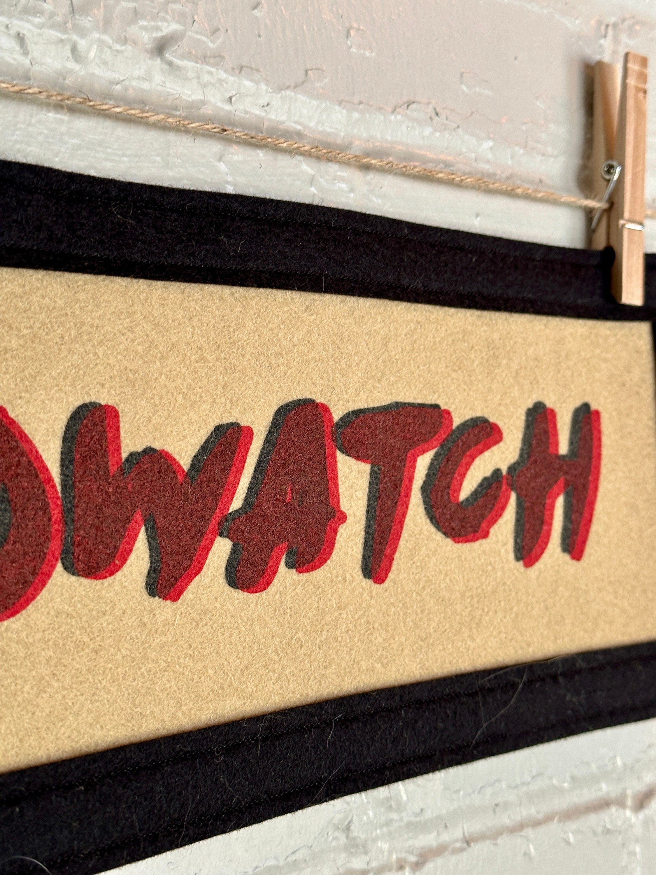 Close up side view of a light brown banner with black trim and double printed red and black lettering reading "BIRDWATCH"