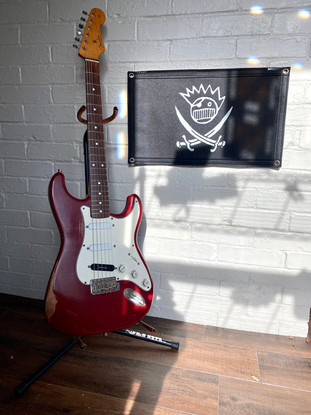 A large black felt banner with a jolly roger boognish design printed in white ink beside a red stratocaster guitar