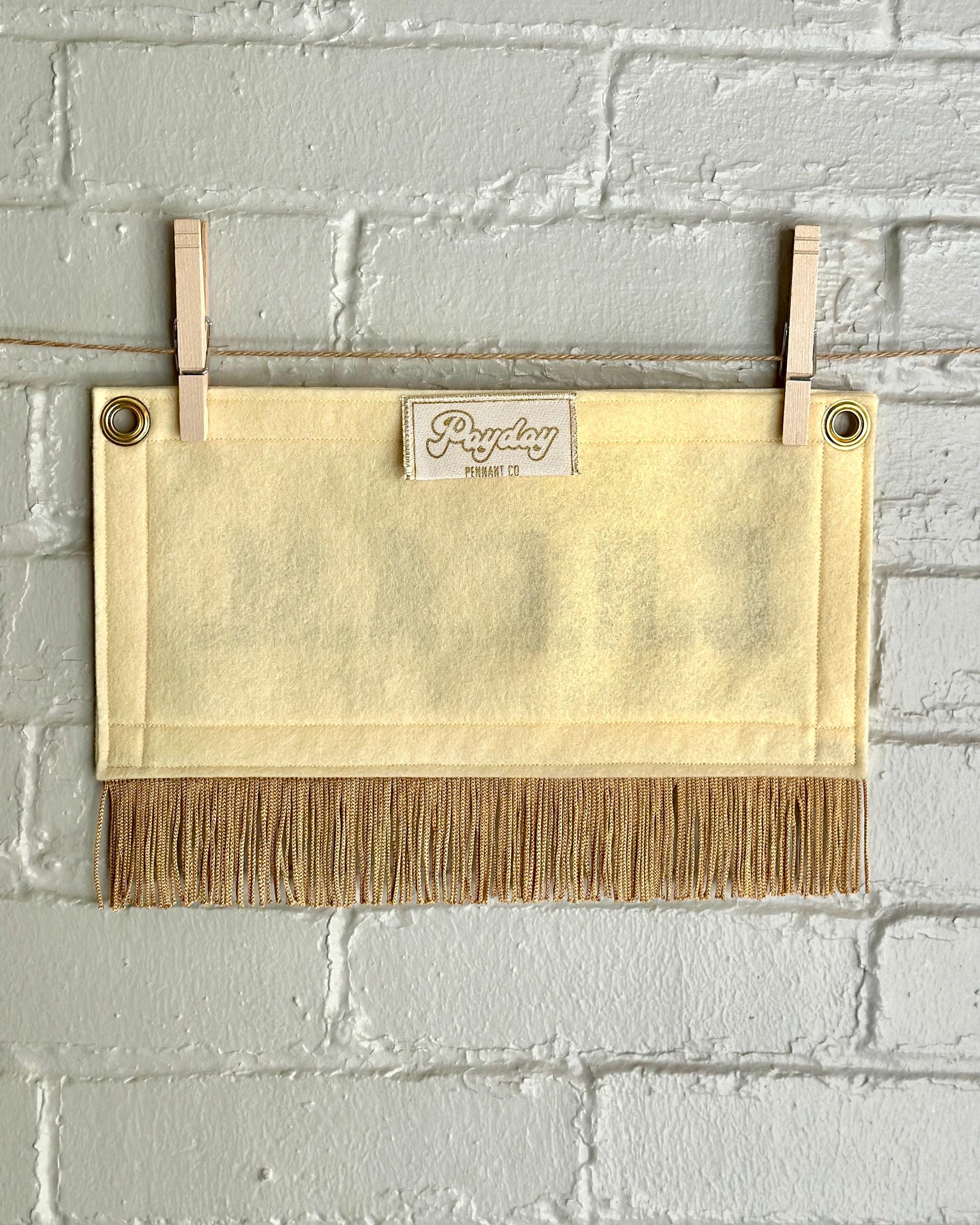 Back of a cream felt banner with cream trim and gold fringe, and gold lettering that reads 'C.R.E.A.M.'