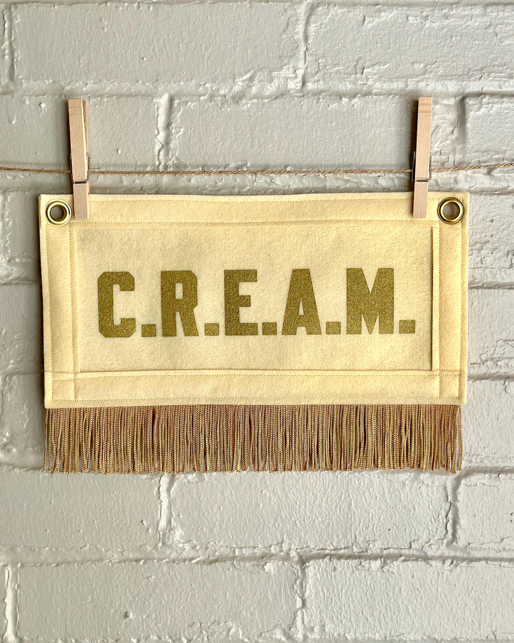 Cream felt banner with cream trim and gold fringe, and gold lettering that reads 'C.R.E.A.M.'