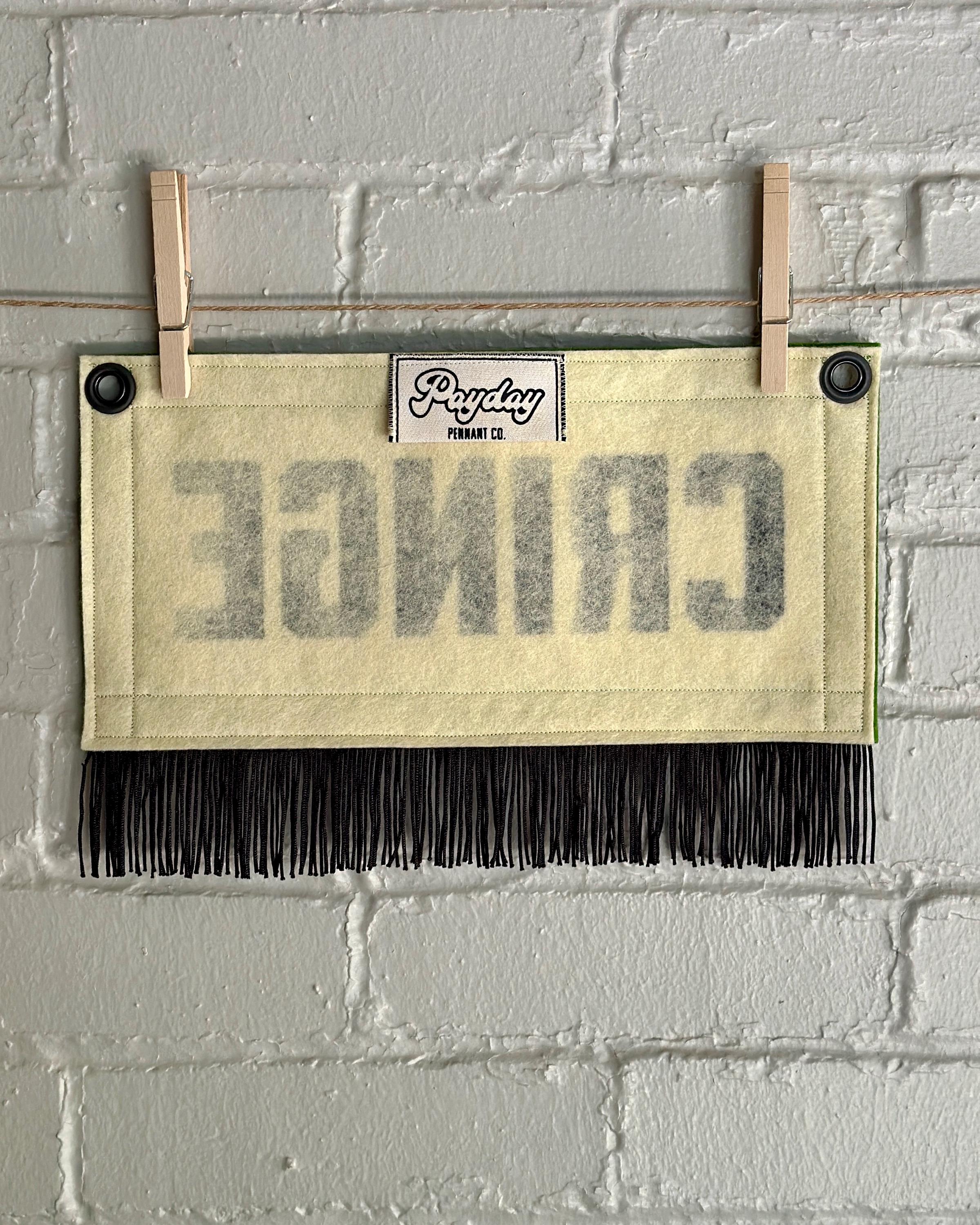 Back of a cream felt banner with green trim, black fringe, and black lettering that reads 'CRINGE'