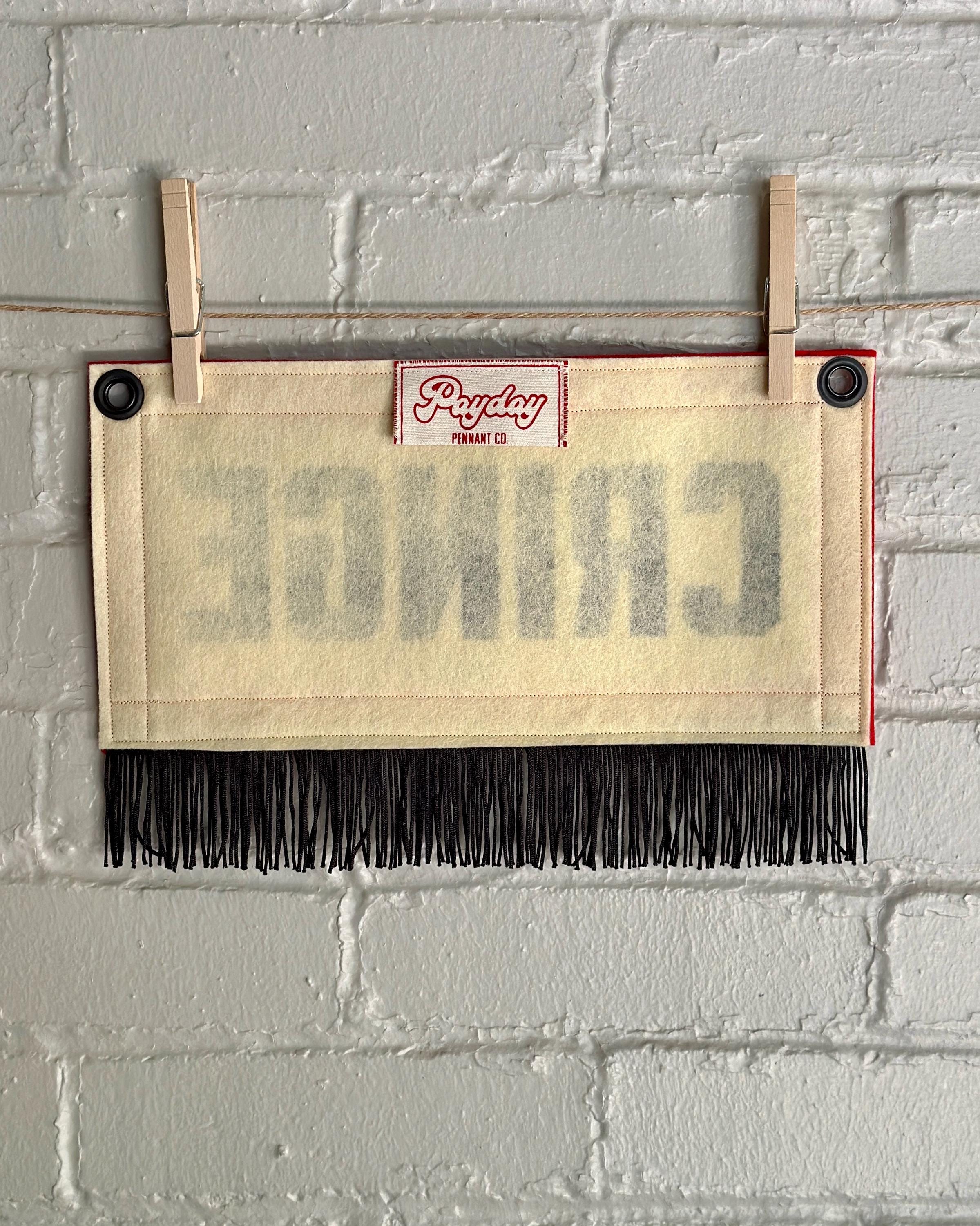 Back of a cream felt banner with red trim, black fringe, and black lettering that reads 'CRINGE'