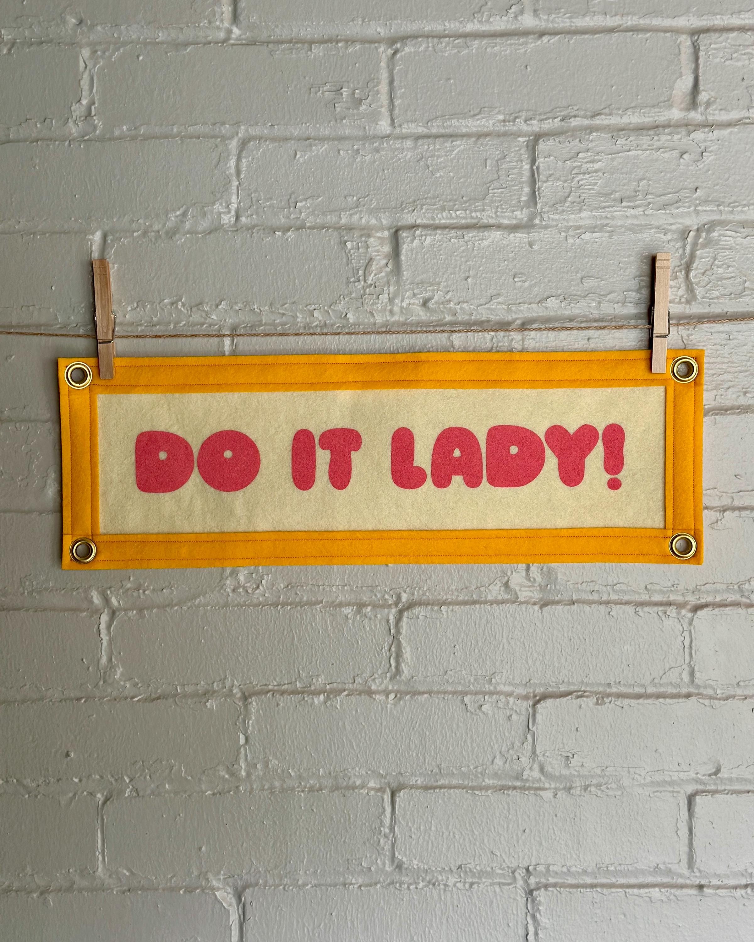 A cream felt banner with yellow trim and pink lettering that reads "Do it lady!"