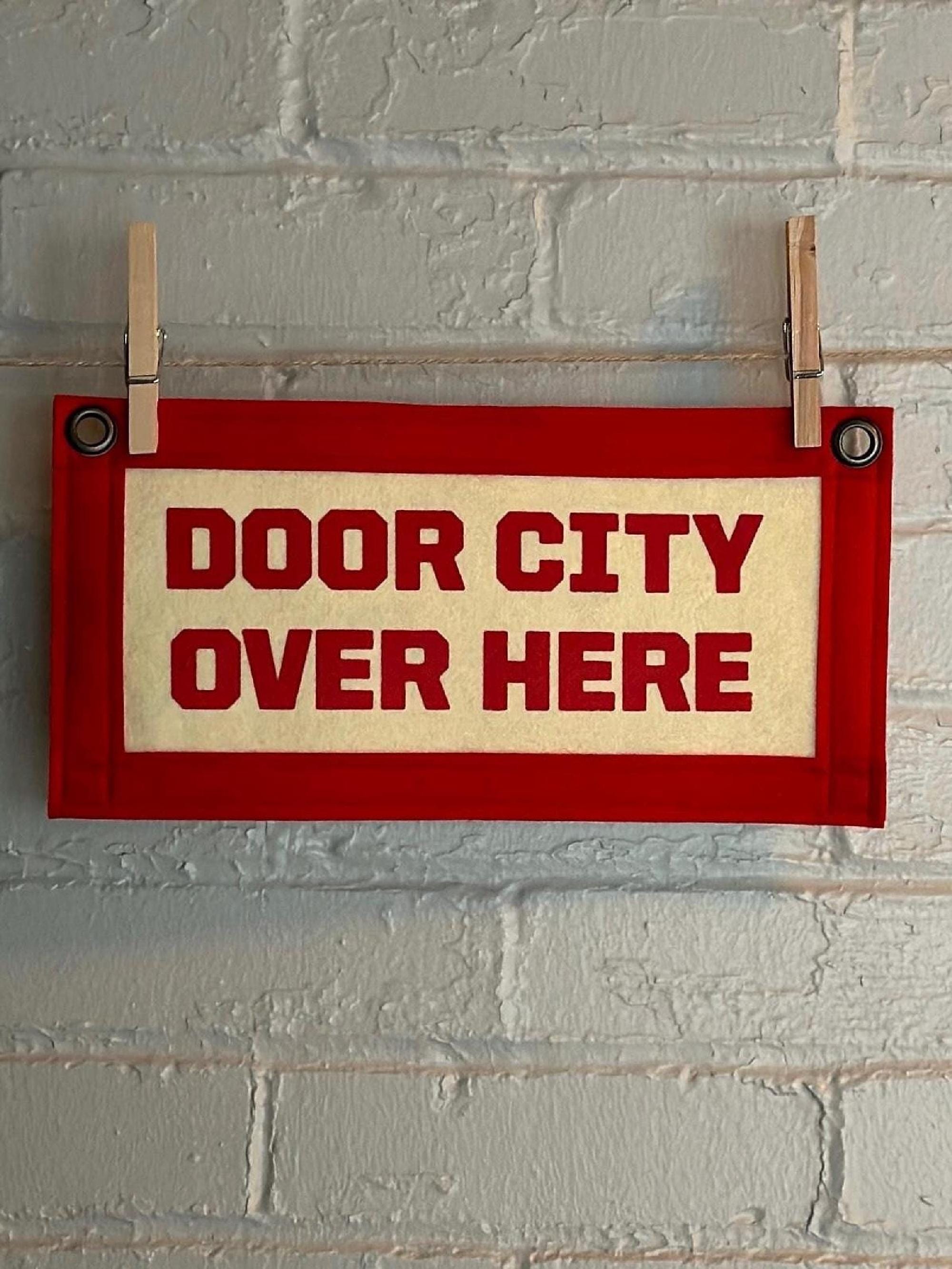 Cream banner with red felt trim and lettering that reads "door city over here"