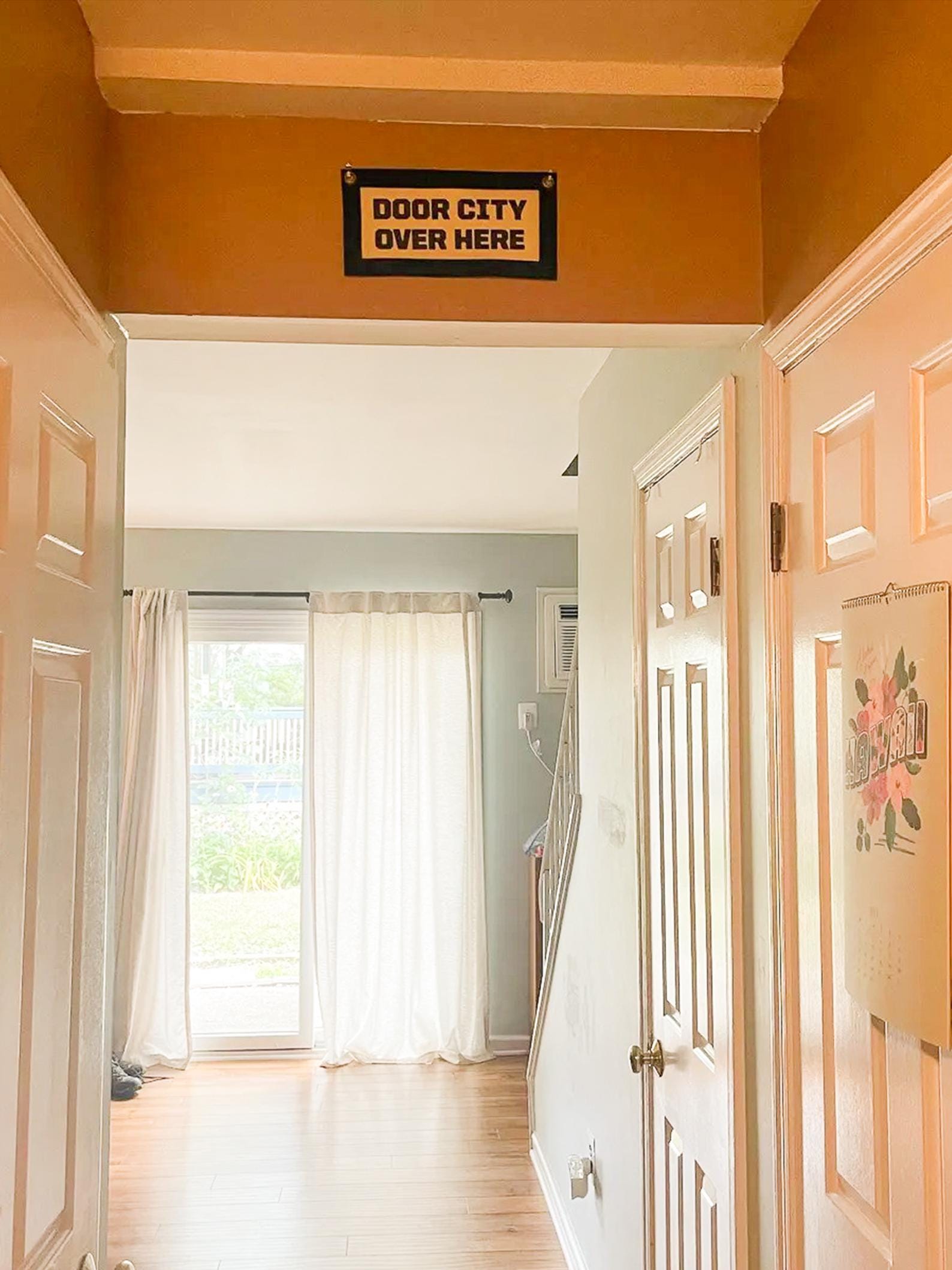 Hallway with a sign on the wall reading 'Door City Over Here' and a view of a room with curtains.