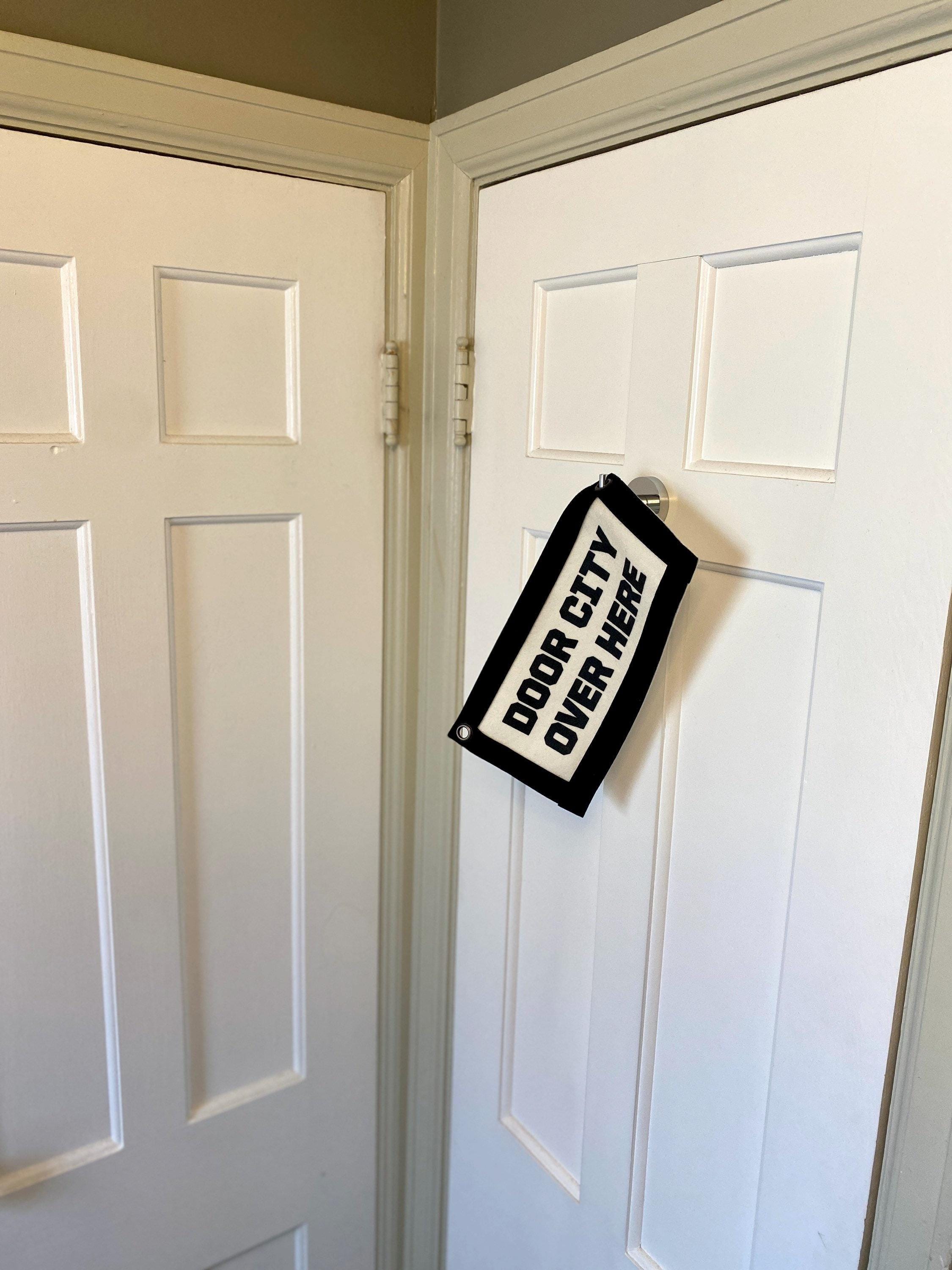 A black felt "door city" banner hanging on a hook from a door, perpendicular to another closed door