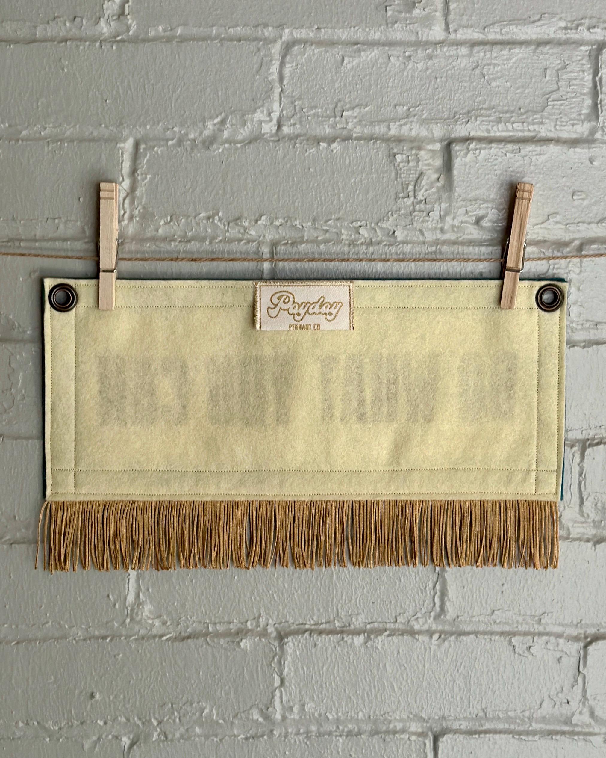 Back of a cream felt banner with blue spruce trim, gold fringe and lettering that reads "Do what you can"