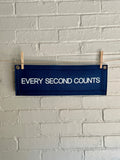 A navy felt banner with navy trim and bright white lettering which reads "every second counts"