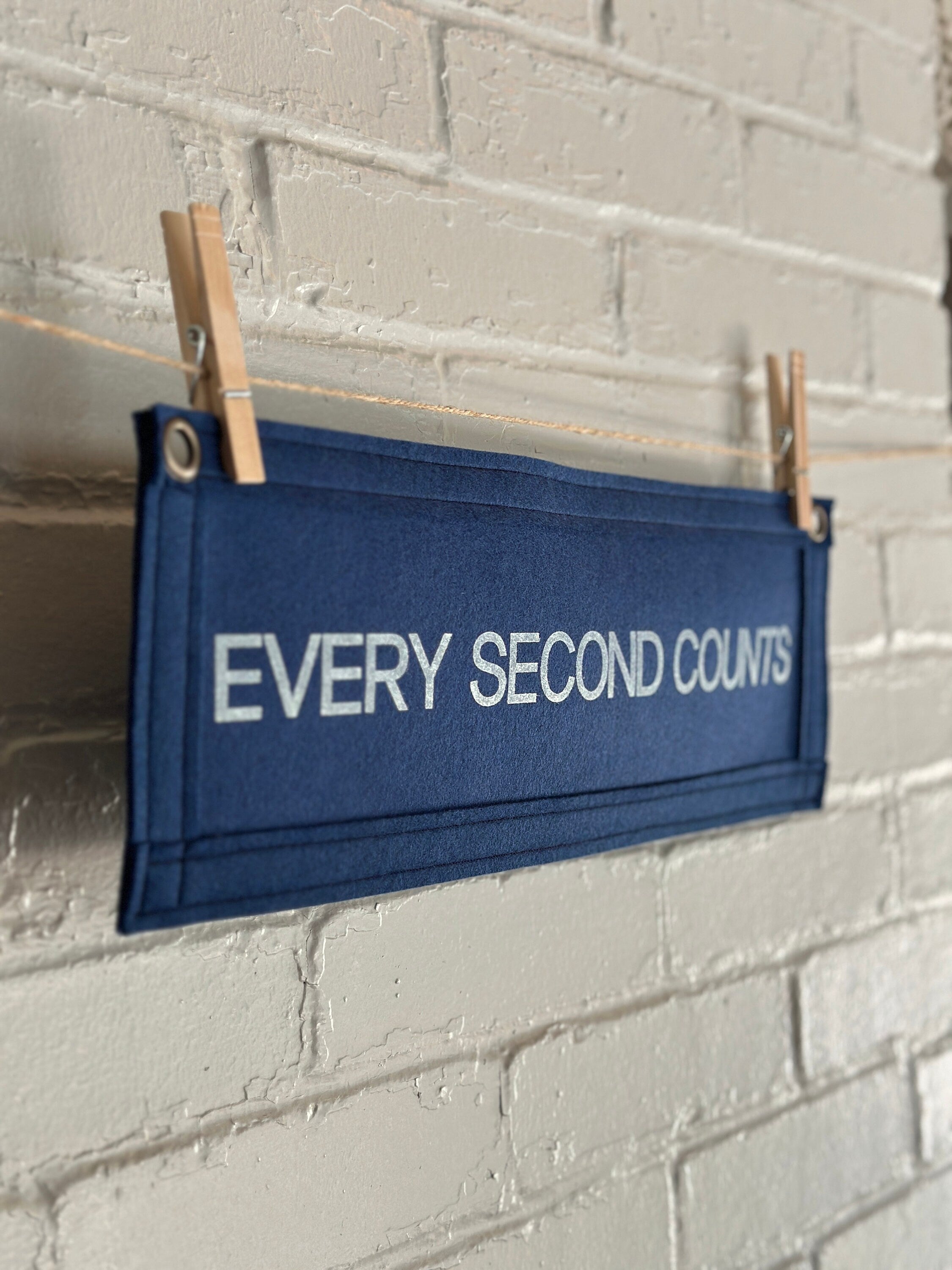 Side view of a navy felt banner with navy trim and bright white lettering which reads "every second counts"
