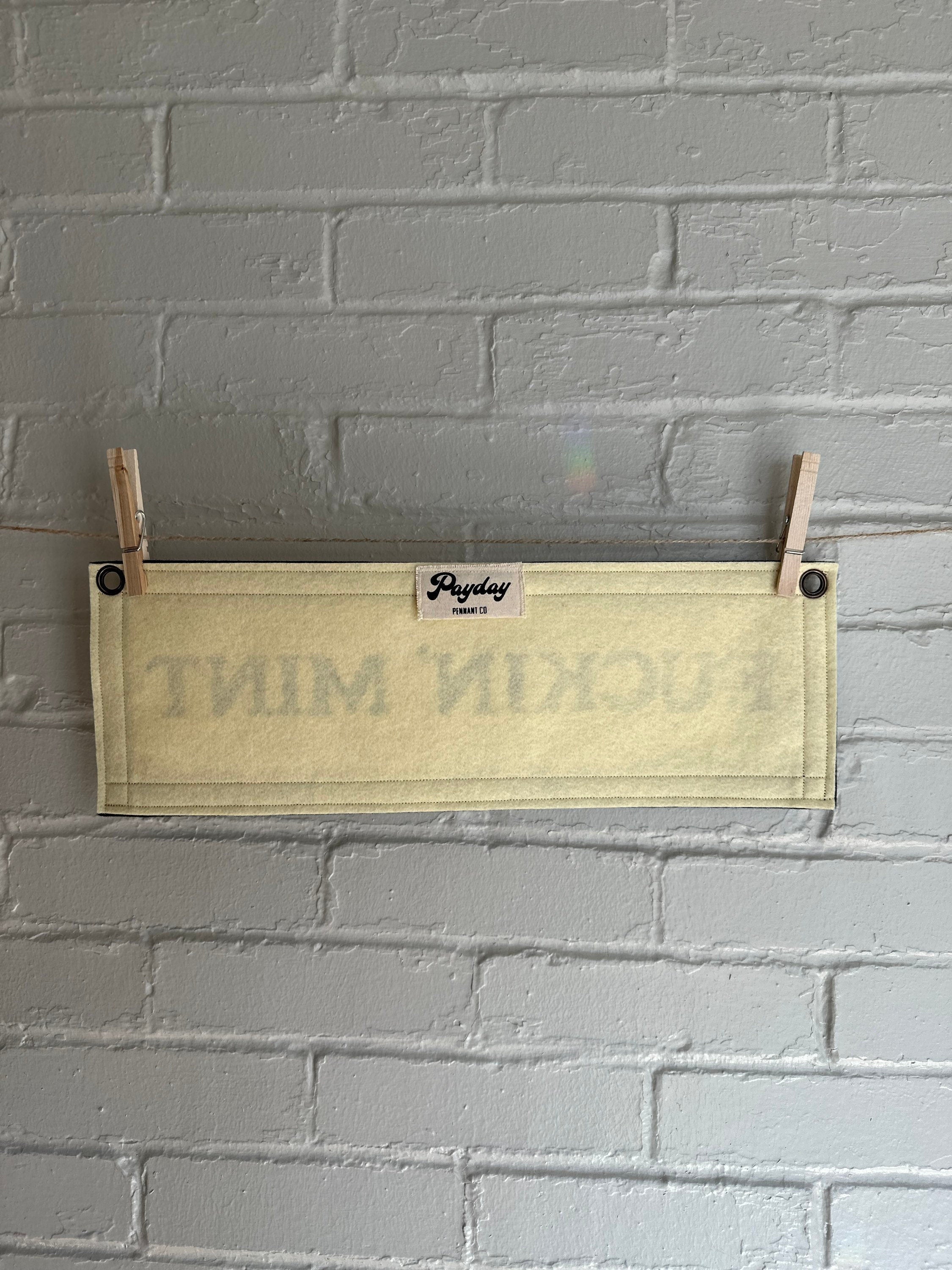 Back of a cream felt banner with black trim and lettering that reads "fuckin' mint"