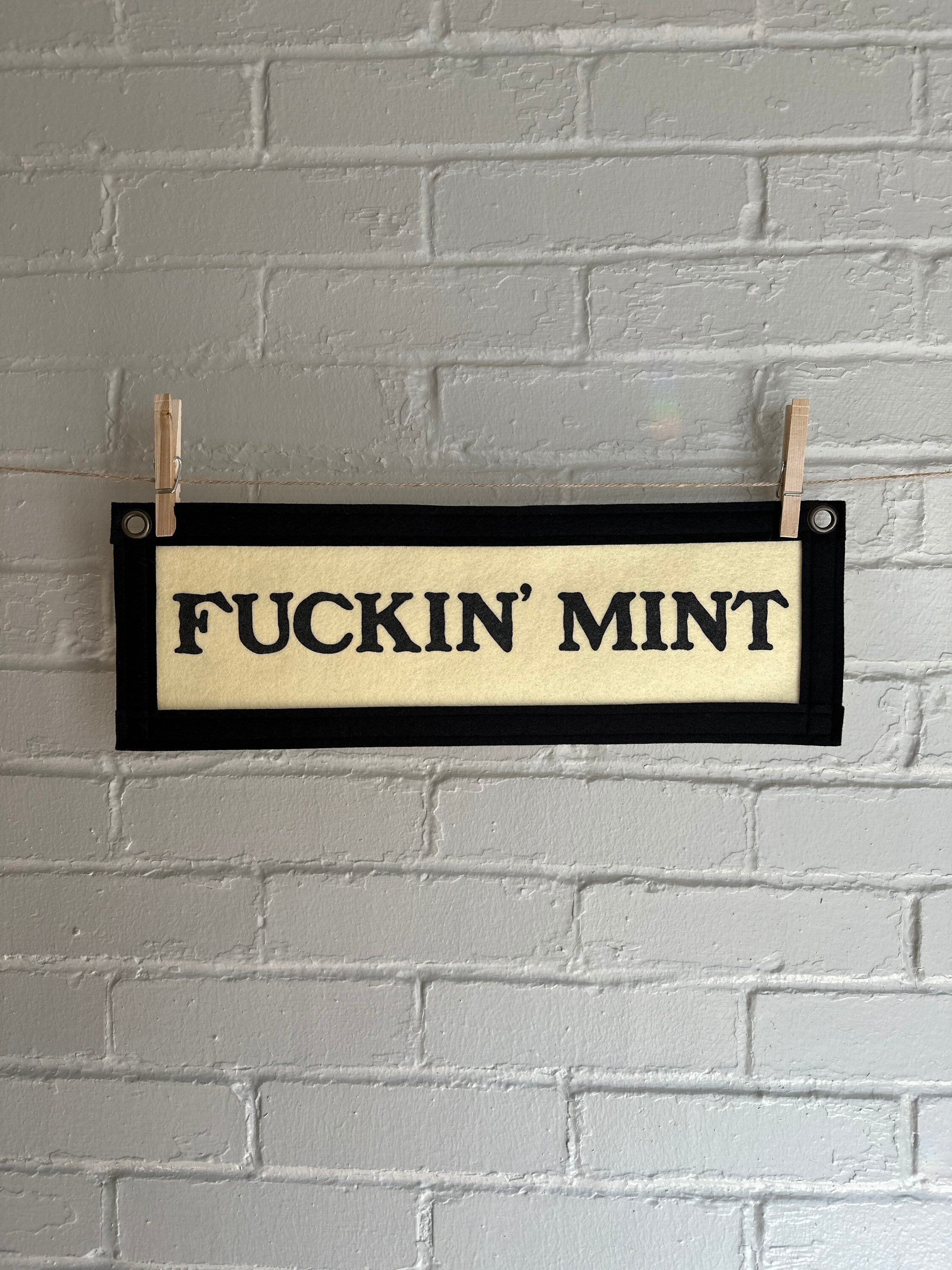 A cream felt banner with black trim and lettering that reads "fuckin' mint"