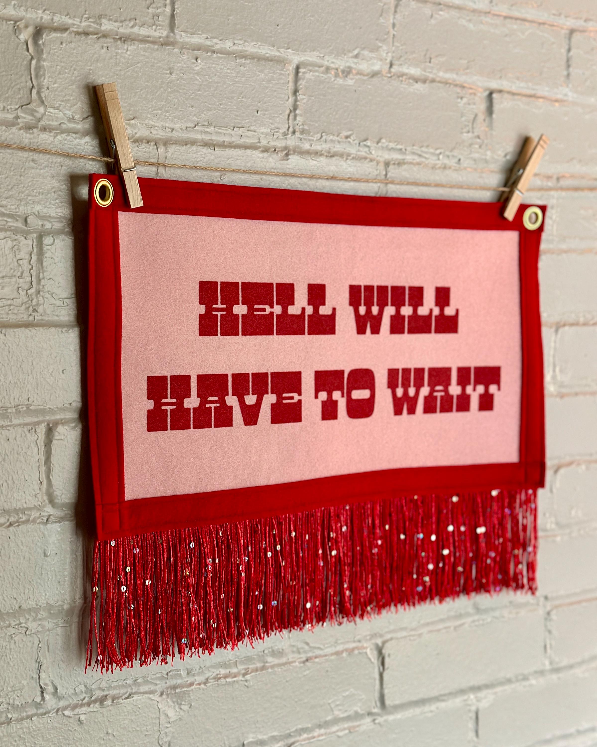 Side view of a cream felt banner with red trim, long red sequin fringe, and red lettering reading "Hell will have to wait"