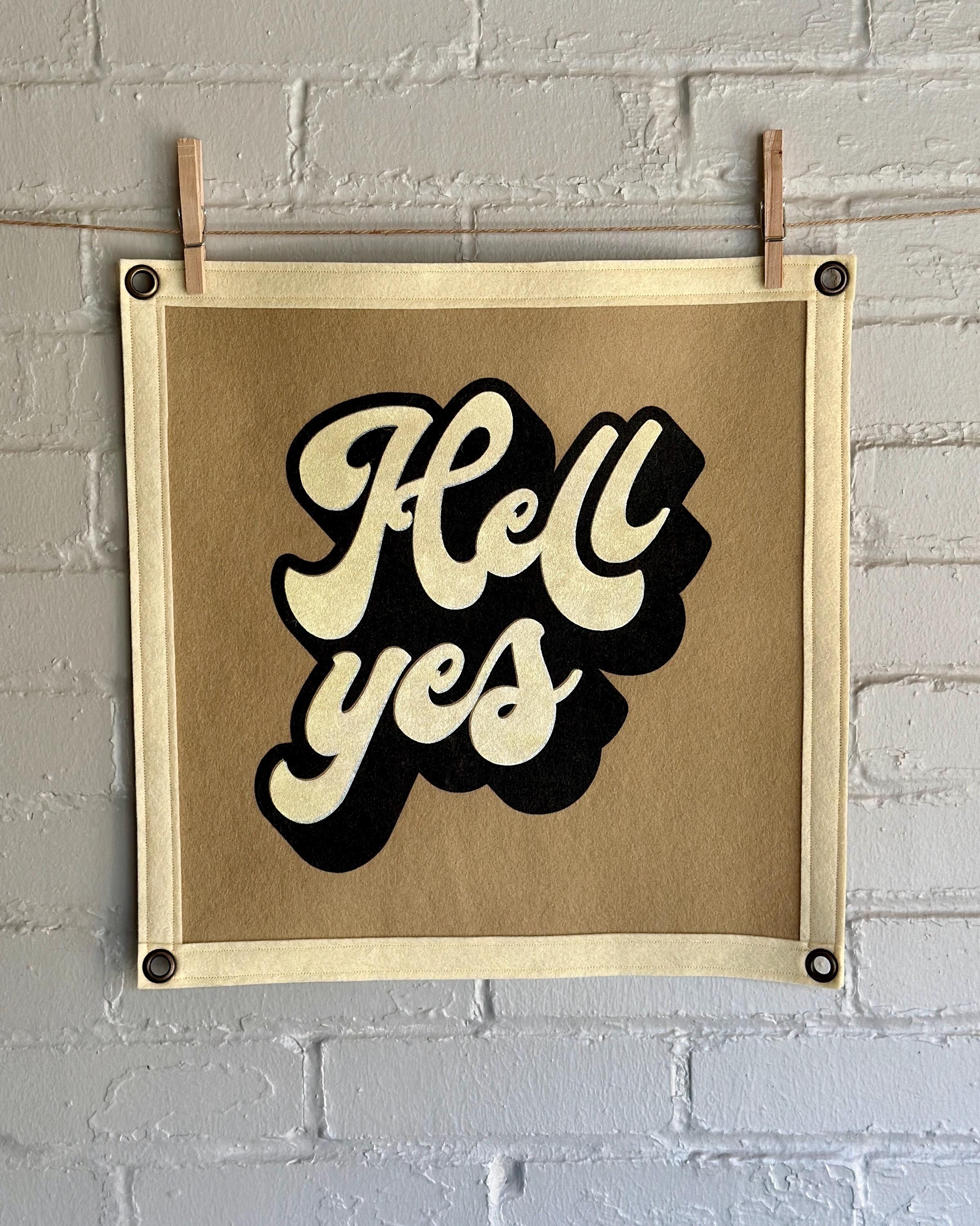 A light brown banner with black trim and a large stylized vintage lettering in black and cream ink that reads "Hell yes"