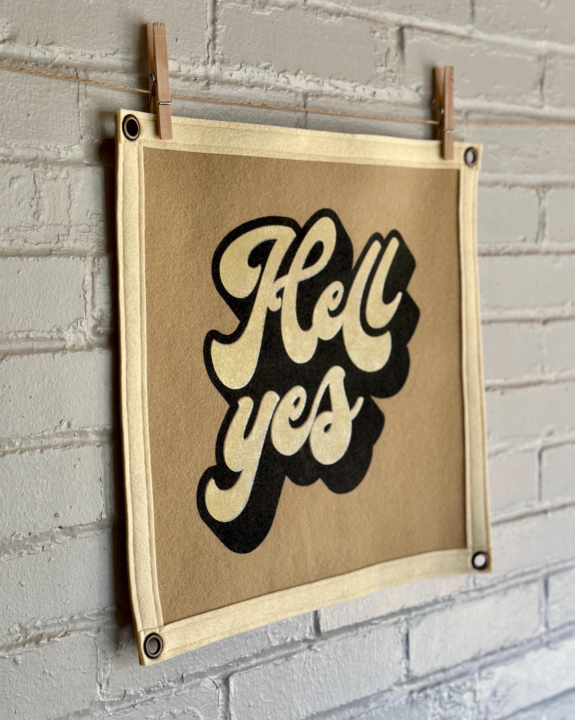 Side view of a light brown banner with black trim and a large stylized vintage lettering in black and cream ink that reads "Hell yes"