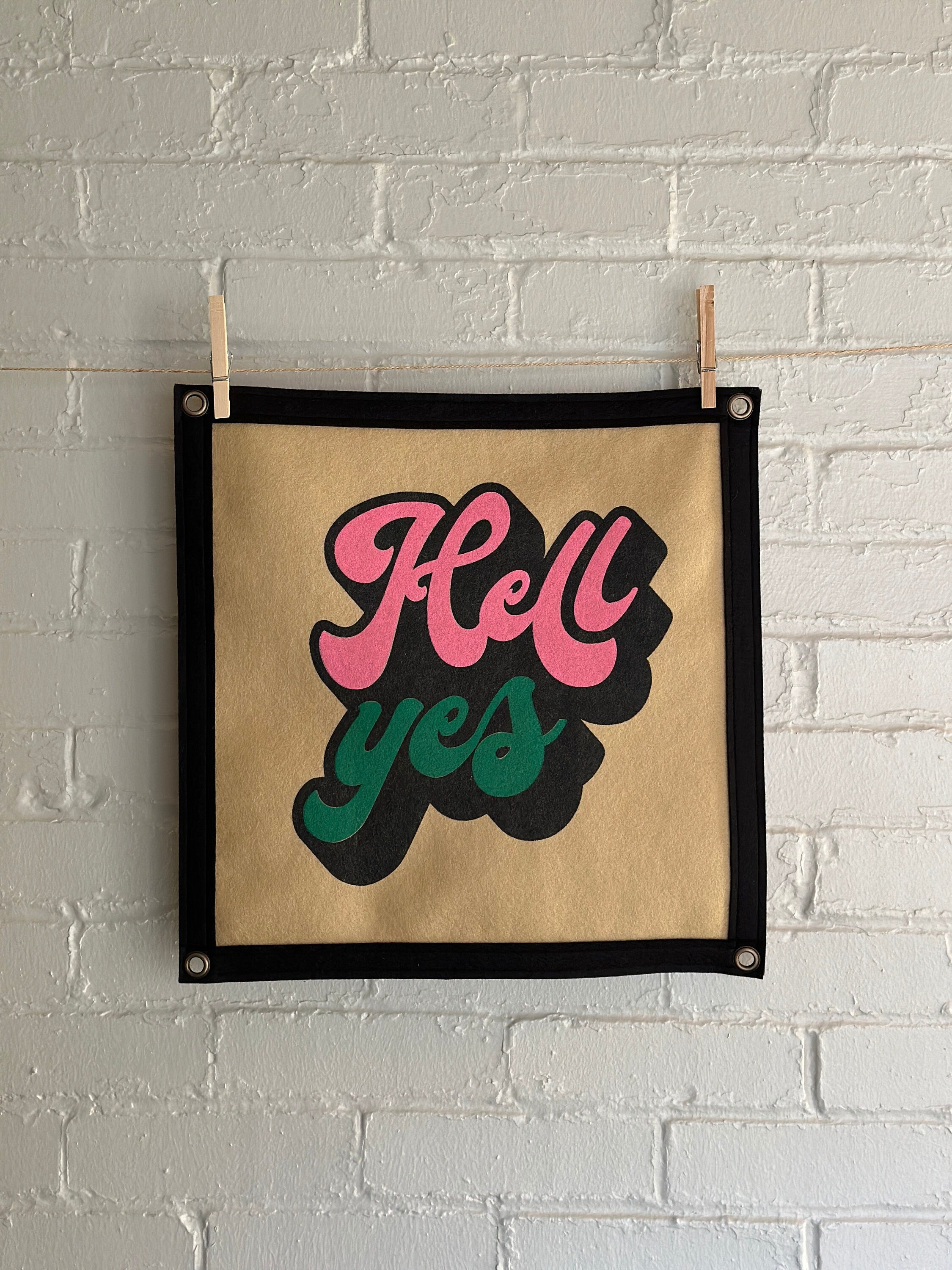 A light brown banner with black trim and a large stylized vintage lettering in black, pink and green ink that reads "Hell yes"