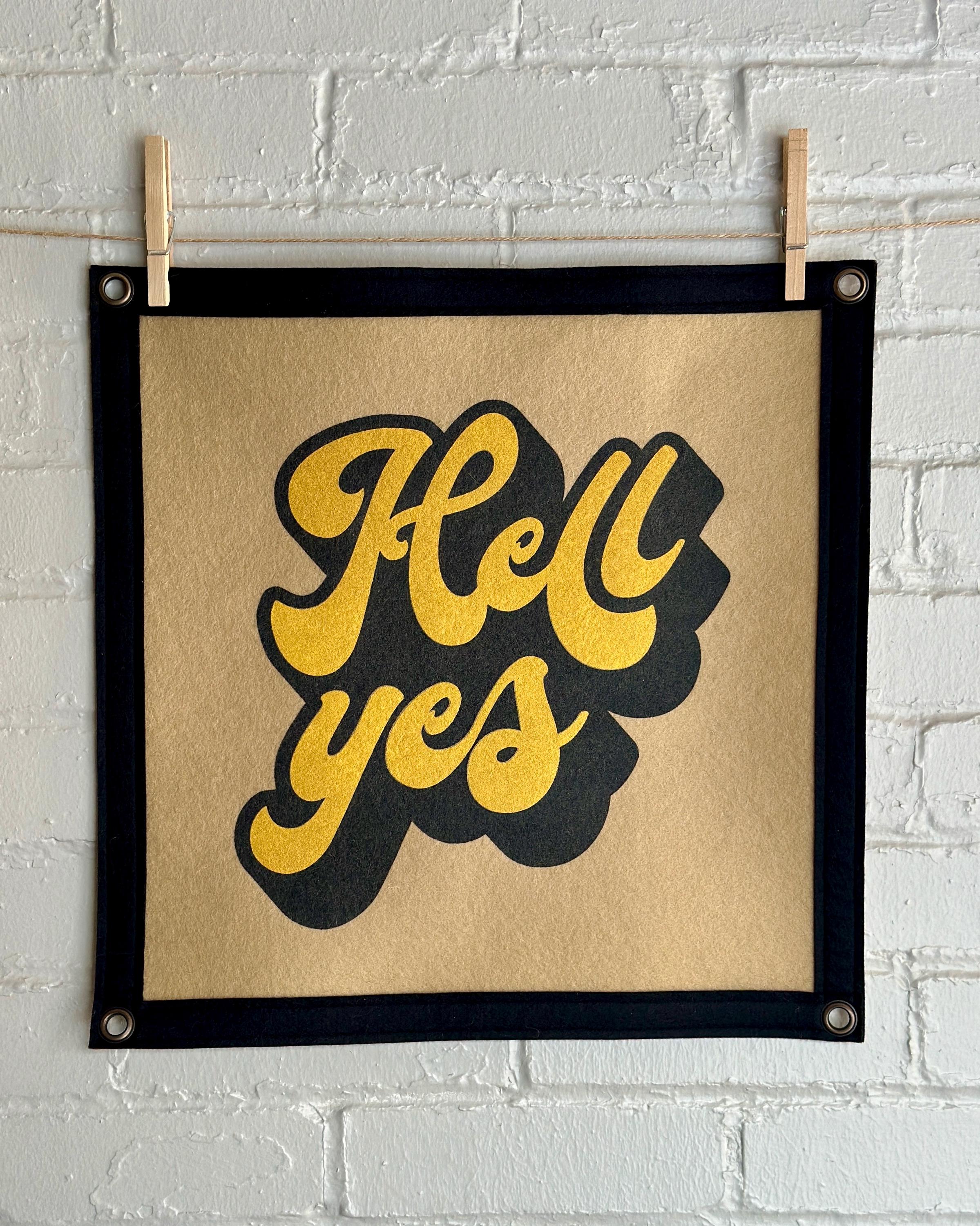 A light brown banner with black trim and a large stylized vintage lettering in black and yellow ink that reads "Hell yes"