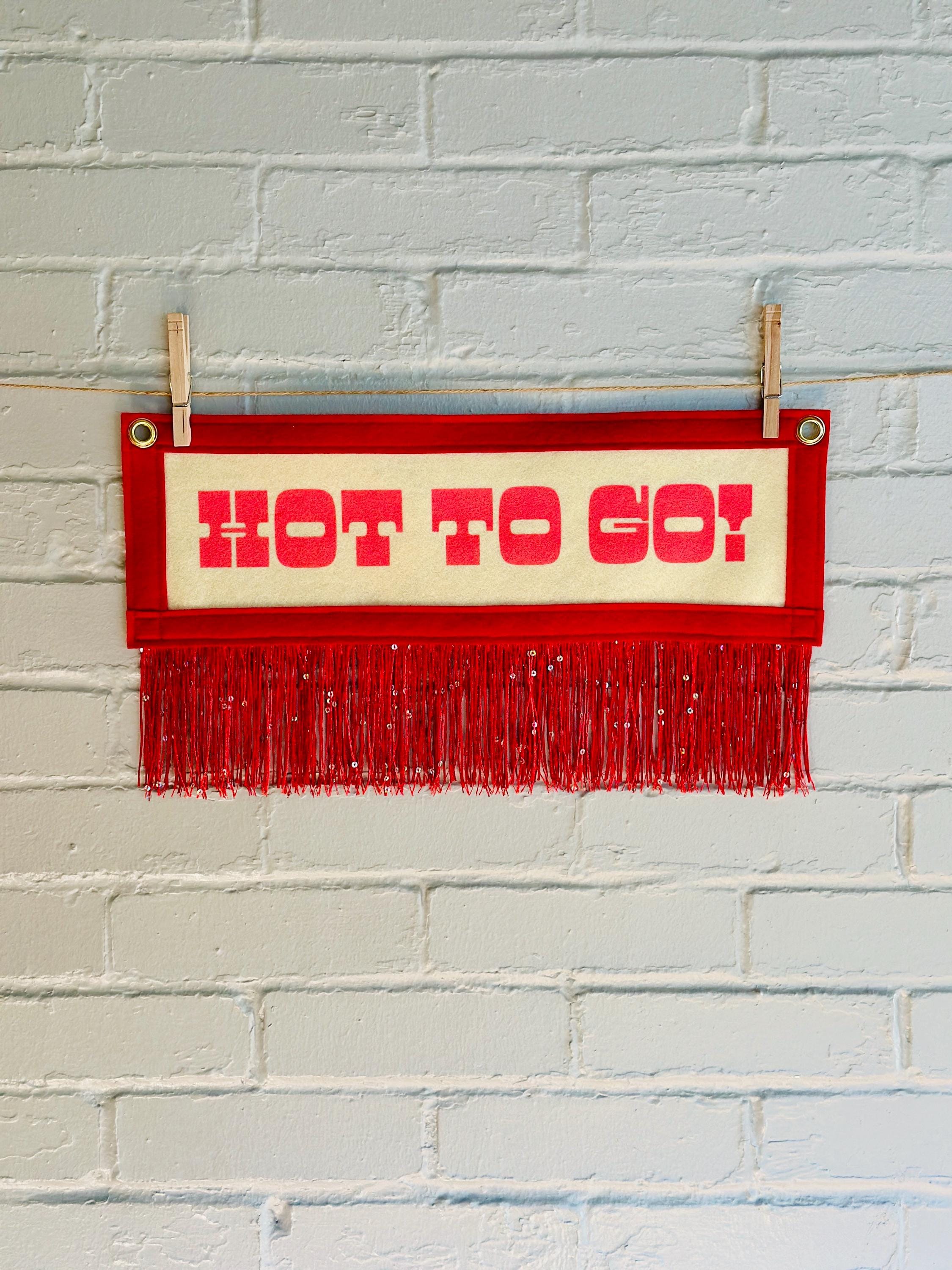 A cream felt banner with red trim and red sequin fringe, pink lettering reads "HOT TO GO!"