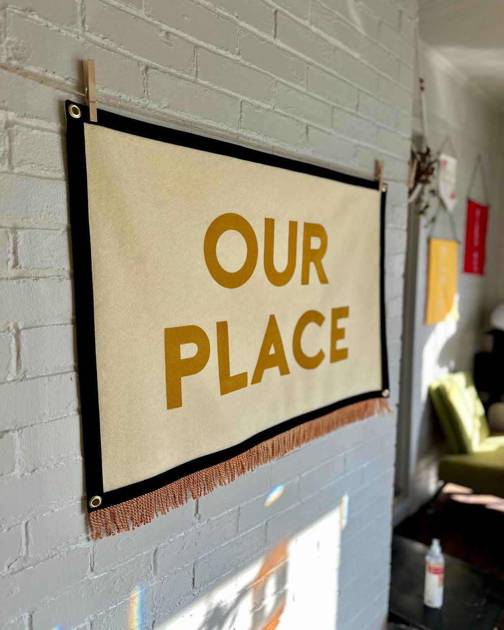 Side view of a large cream felt banner with black trim, gold bullion fringe, and letters in yellow ink that read "OUR PLACE"