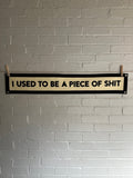 A cream banner with black trim and lettering that reads "I used to be a piece of shit"