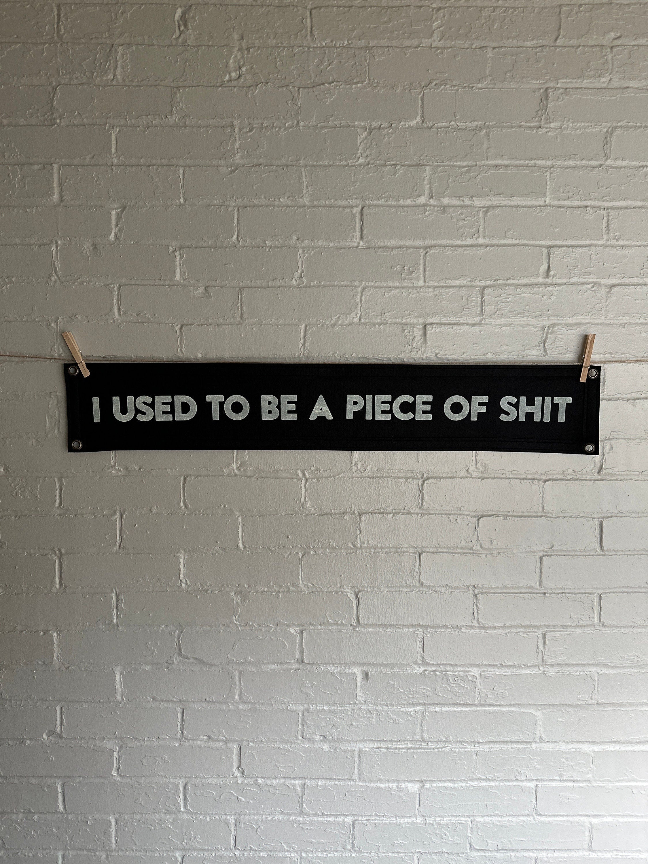A black banner with black trim and white lettering that reads "I used to be a piece of shit"