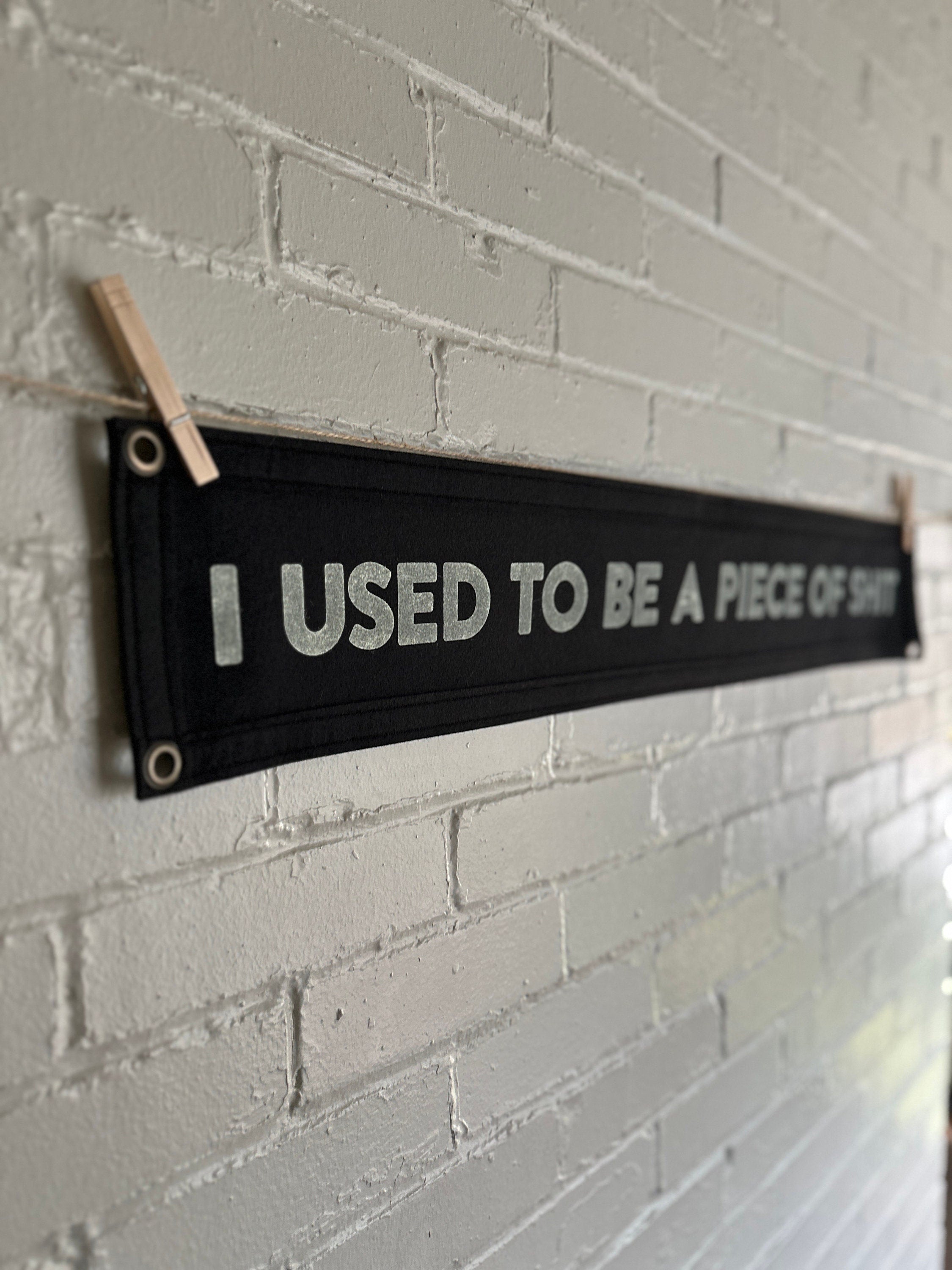 Side view of a black banner with black trim and white lettering that reads "I used to be a piece of shit"