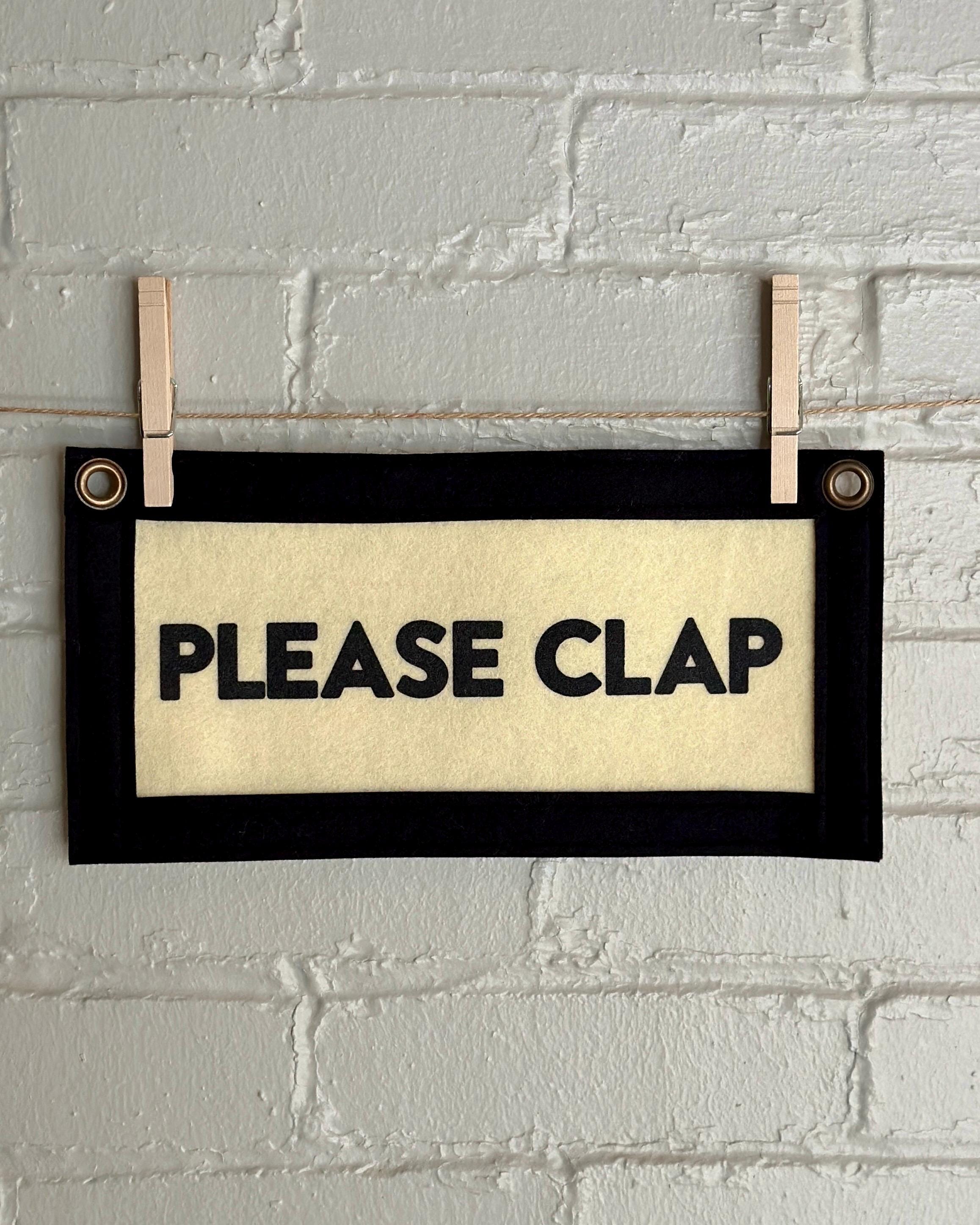 A cream felt banner with black trim and lettering that reads "PLEASE CLAP"