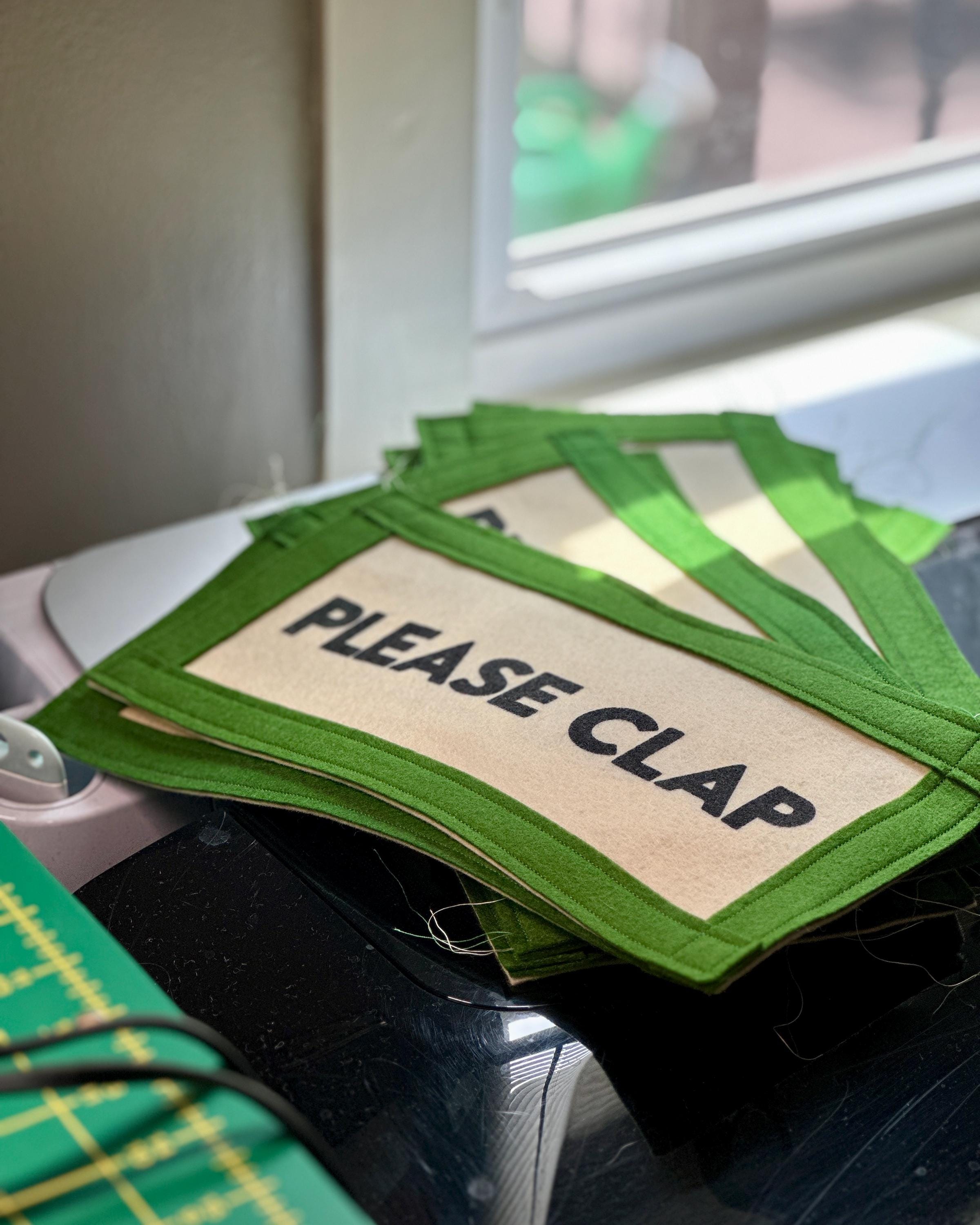 A stack of nearly-finished "Please clap" banners stacked by a desk