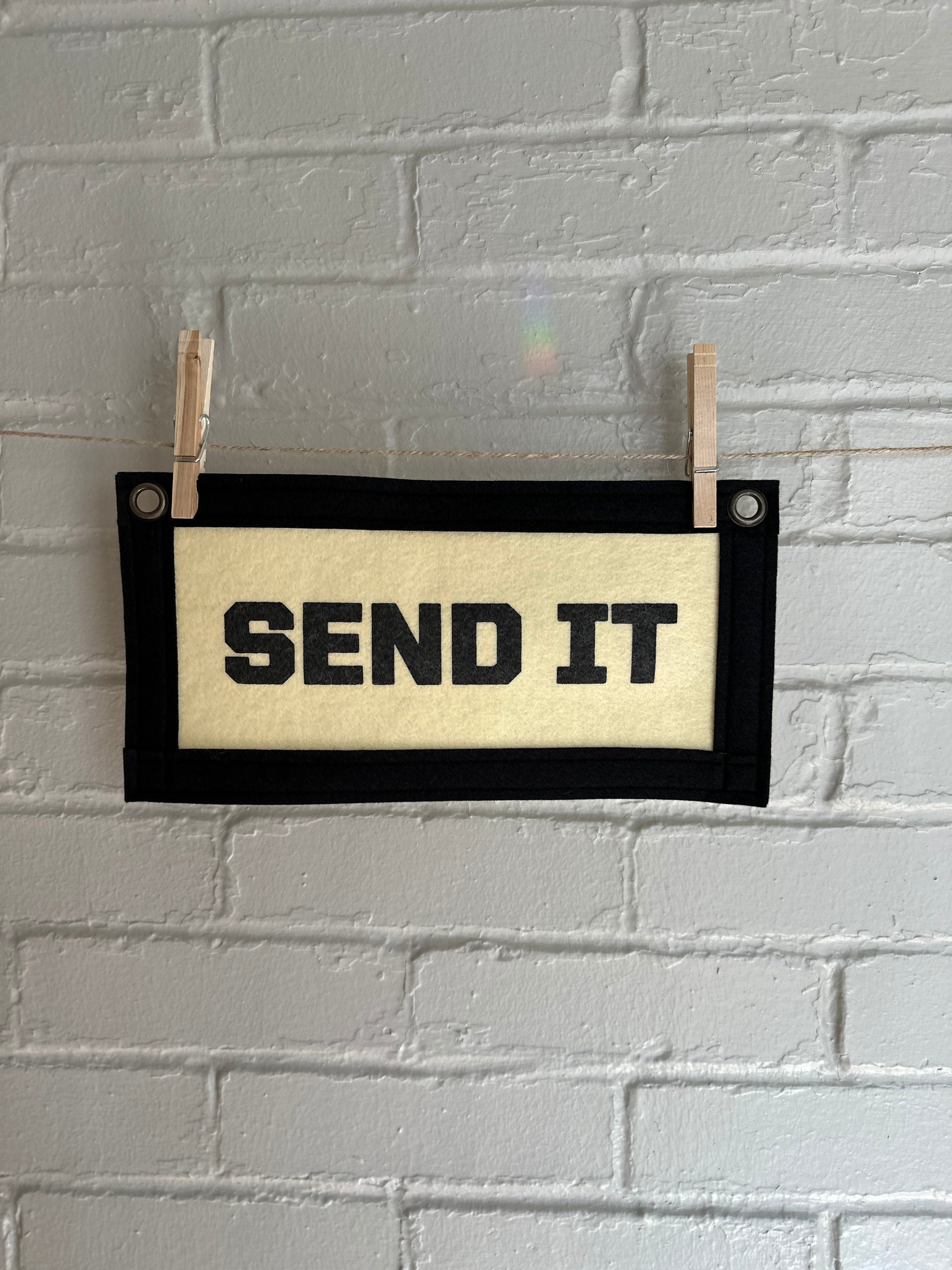 Cream felt banner with black trim and lettering that reads "SEND IT"