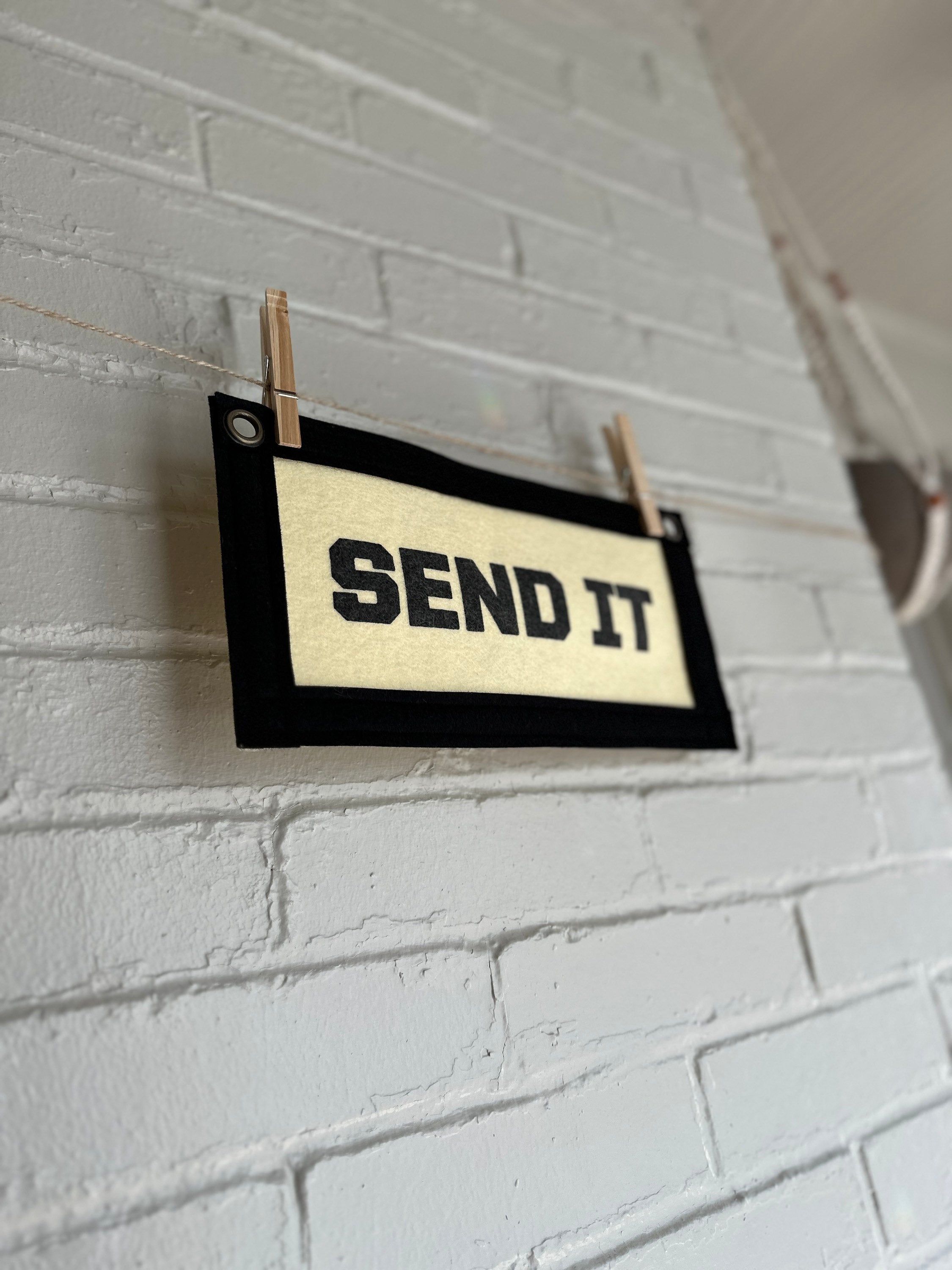 Side view of a cream felt banner with black trim and lettering that reads "SEND IT"