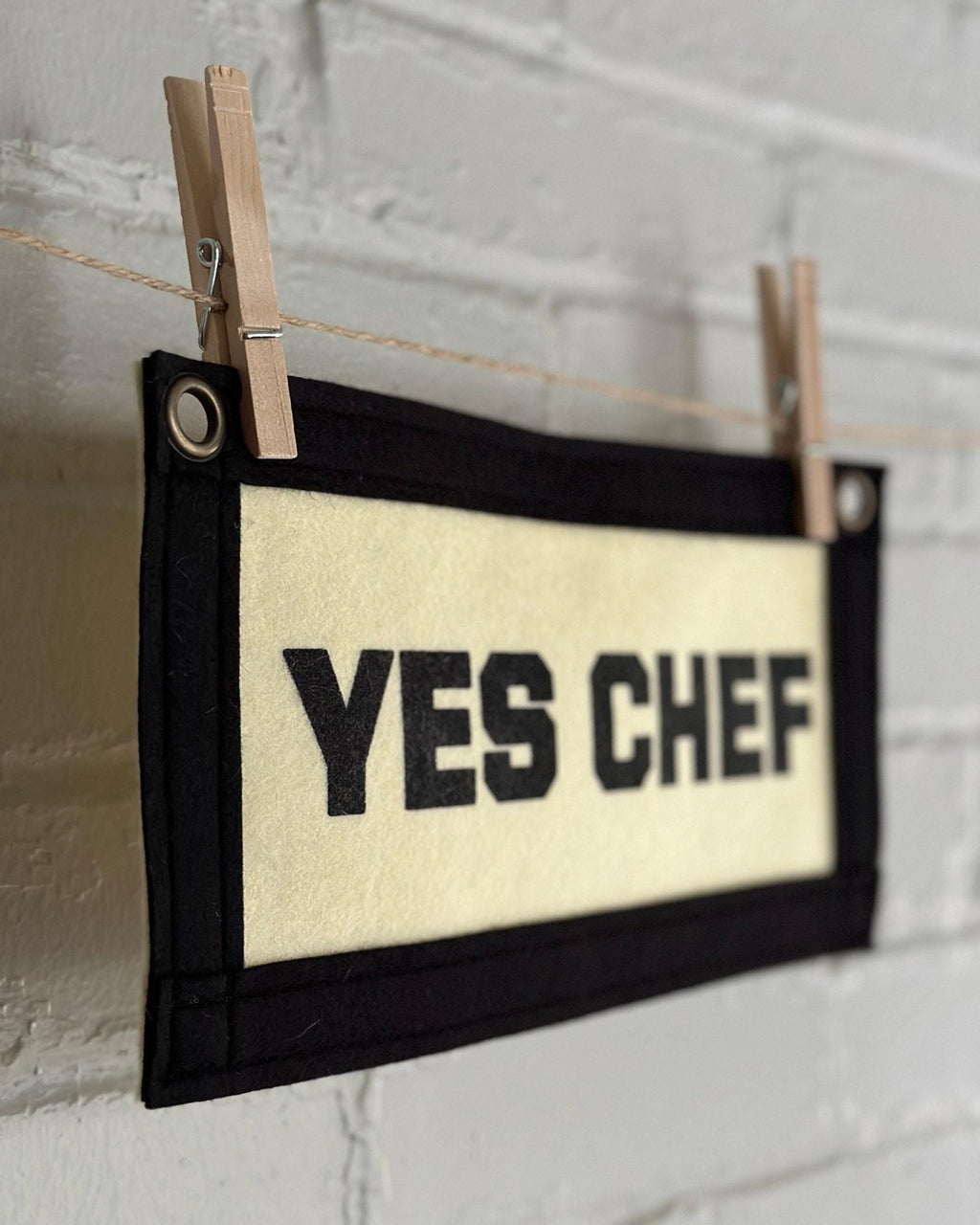 Side view of a cream felt banner with black trim and black print reading "YES CHEF"