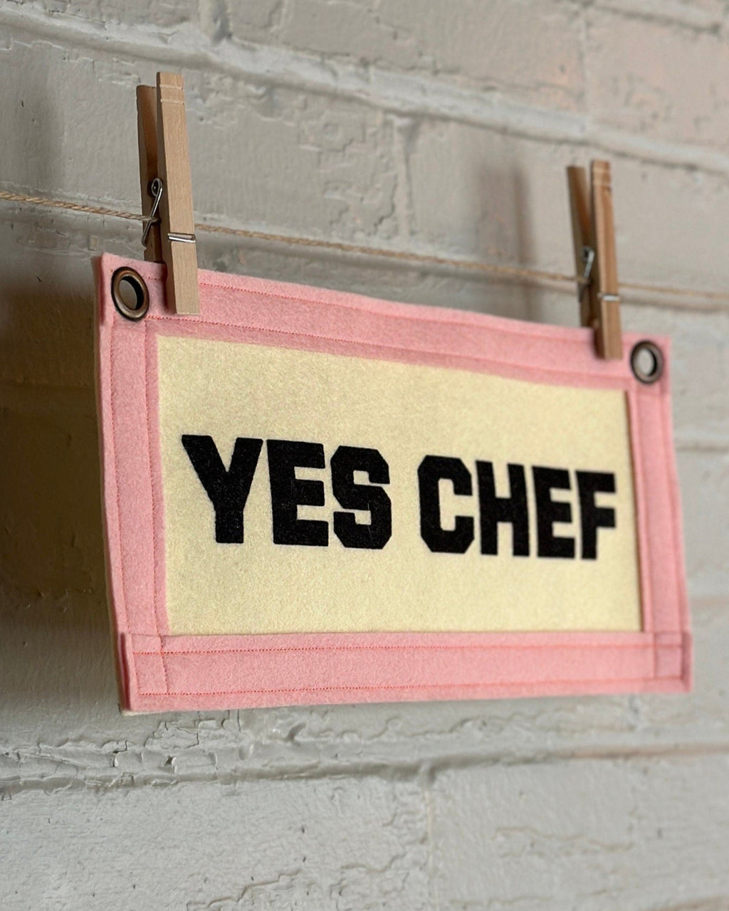 Side view of a cream felt banner with pink trim and black print reading "YES CHEF"