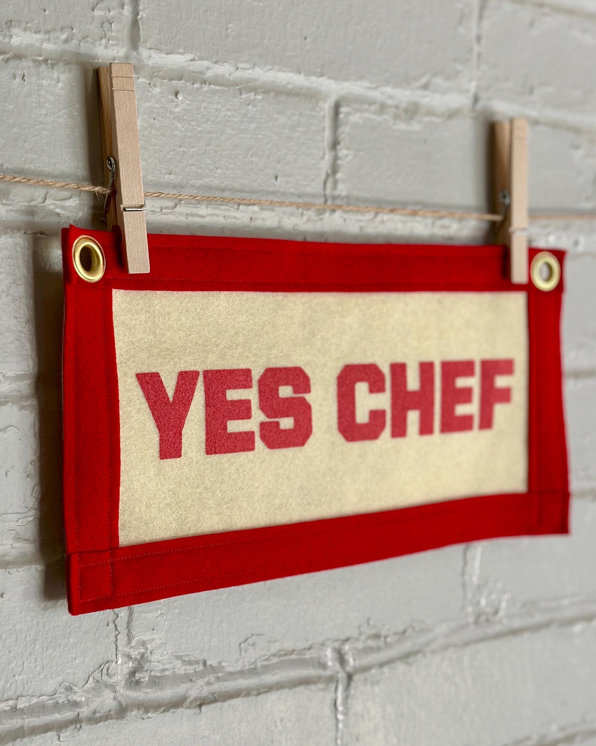 Side view of a cream felt banner with red trim and pink print reading "YES CHEF"