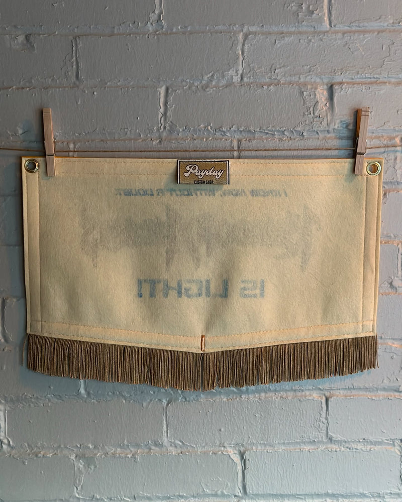 The back of a cream colored pentagonal felt banner with gold fringe and a Payday Custom Shop tag.