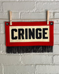 A small felt banner with cream base, red trim and black fringe at the bottom. It reads CRINGE in large letters with black ink.