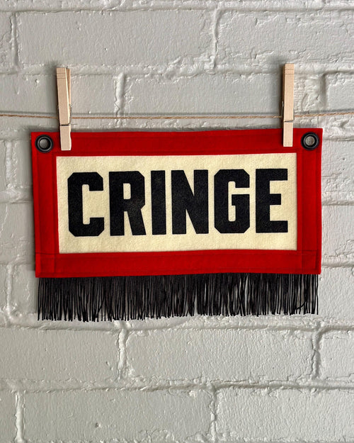 A small felt banner with cream base, red trim and black fringe at the bottom. It reads CRINGE in large letters with black ink.