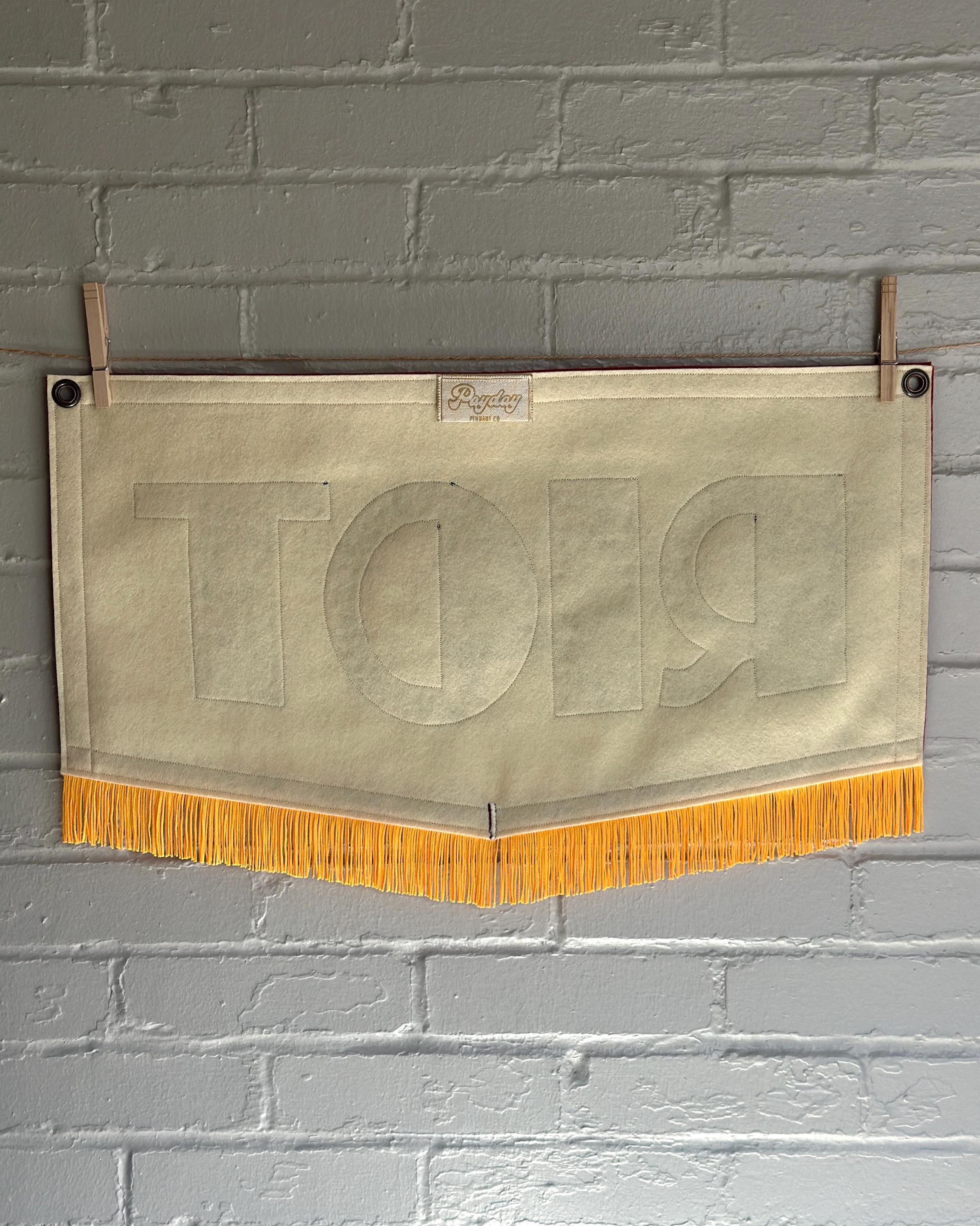 A red, white and blue felt banner with flag gold trim and appliqué letters that read RIOT