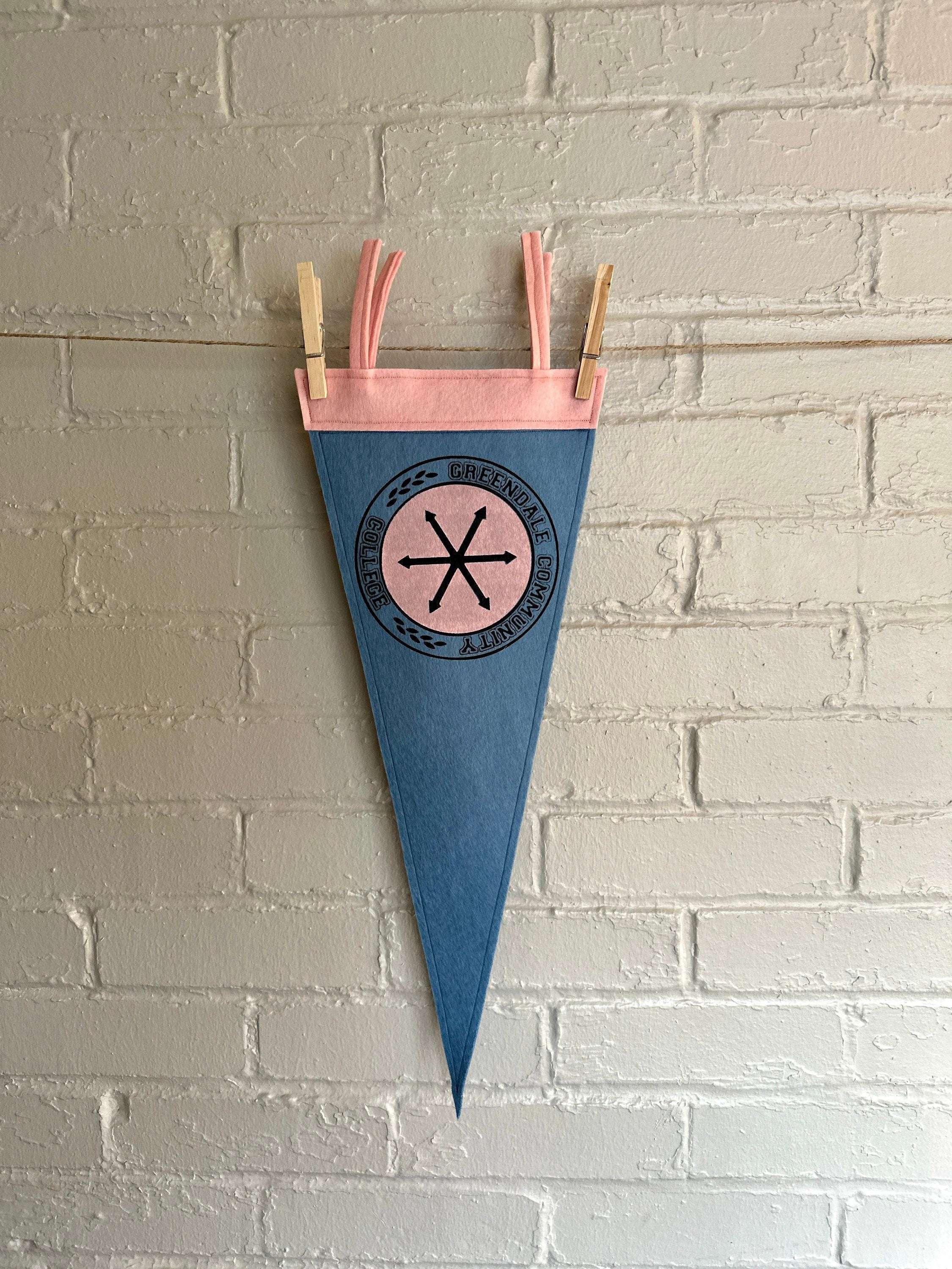 A light blue felt pennant with pink trim and a Greendale Community College logo printed on
