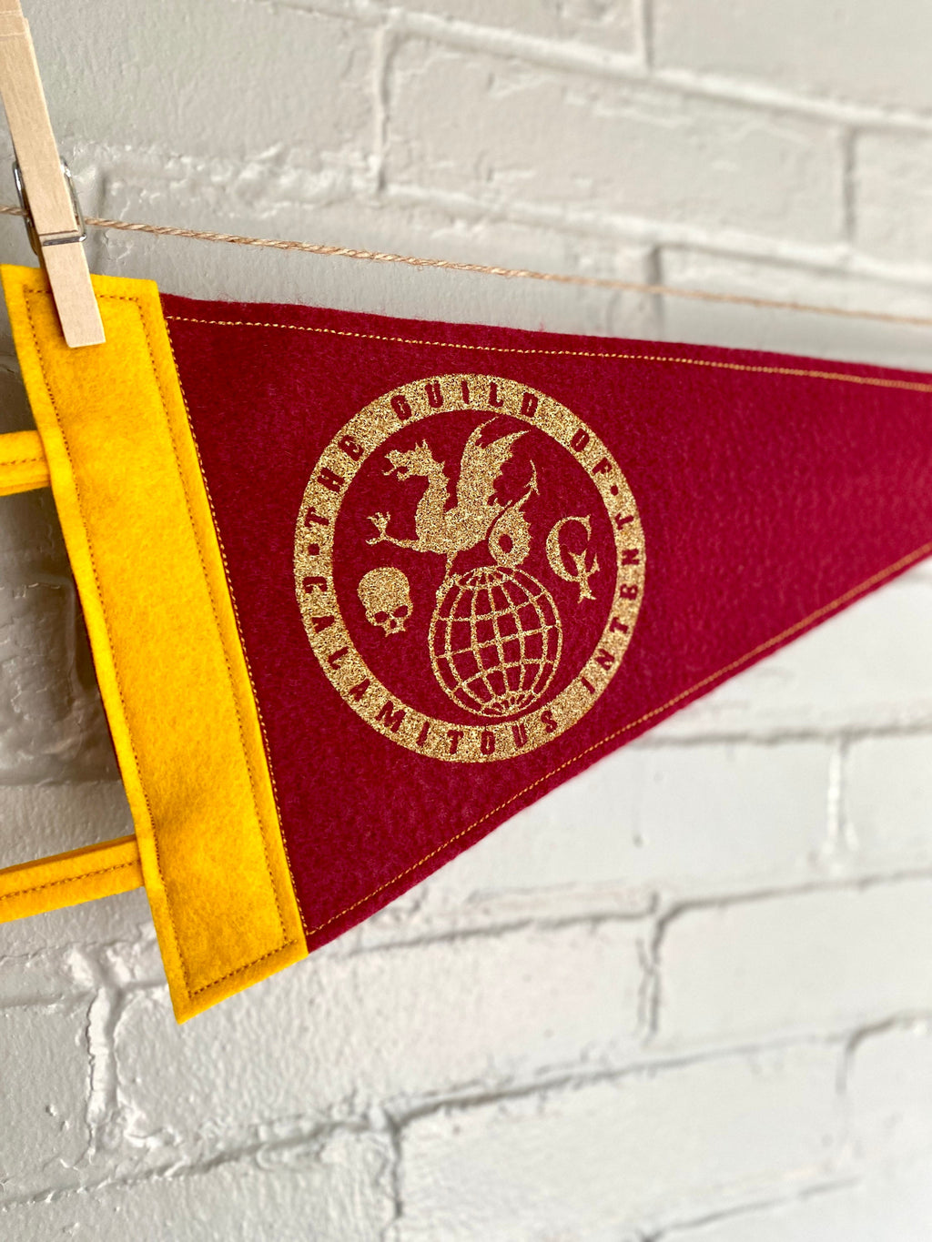 Closeup of a burgundy pennant with yellow felt trim and the Guild of Calamitous Intent logo printed in gold