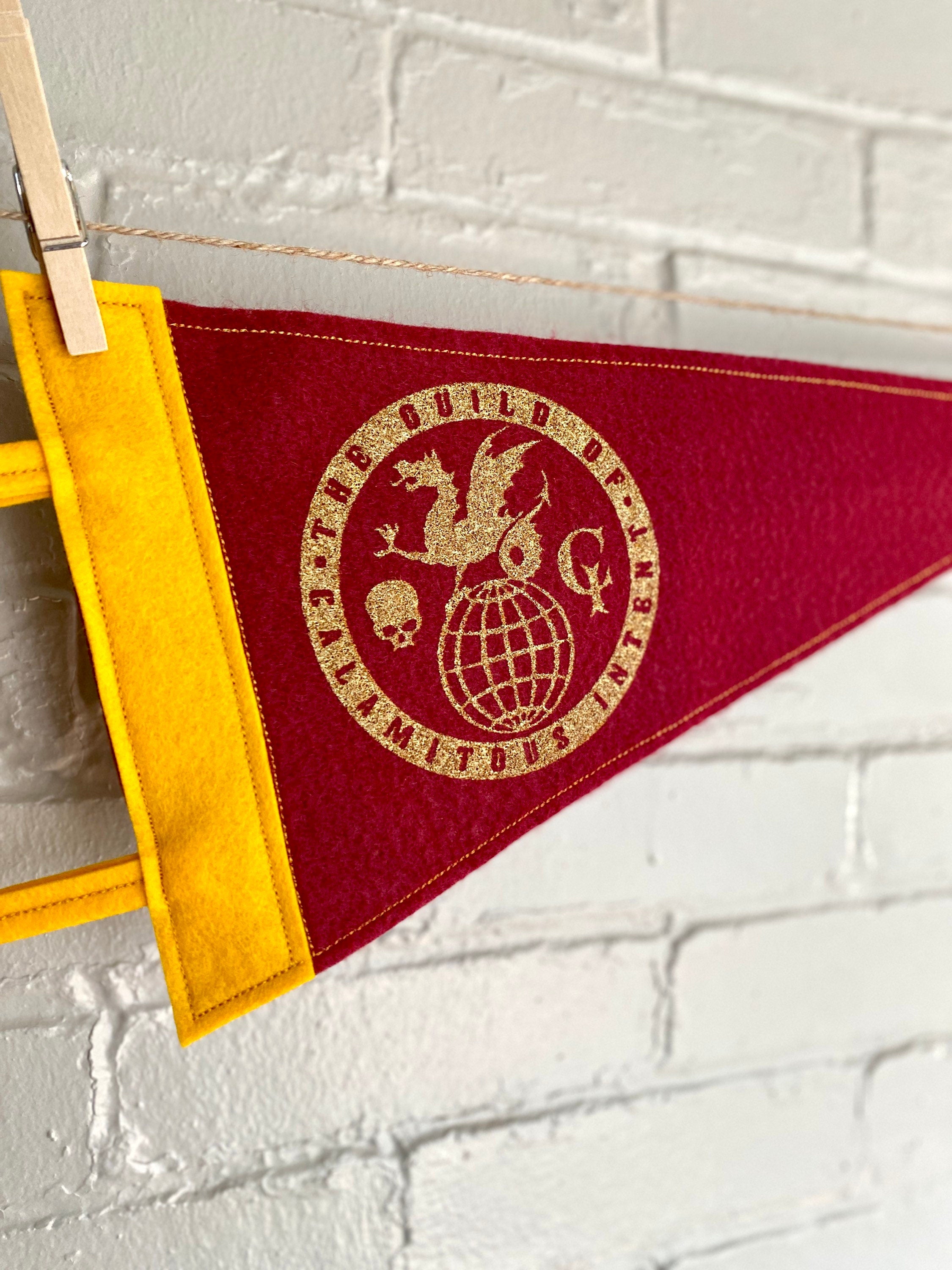 Closeup of a burgundy pennant with yellow felt trim and the Guild of Calamitous Intent logo printed in gold