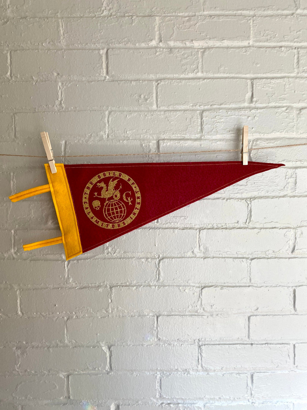 A burgundy pennant with yellow felt trim and the Guild of Calamitous Intent logo printed in gold, hanging horizontally