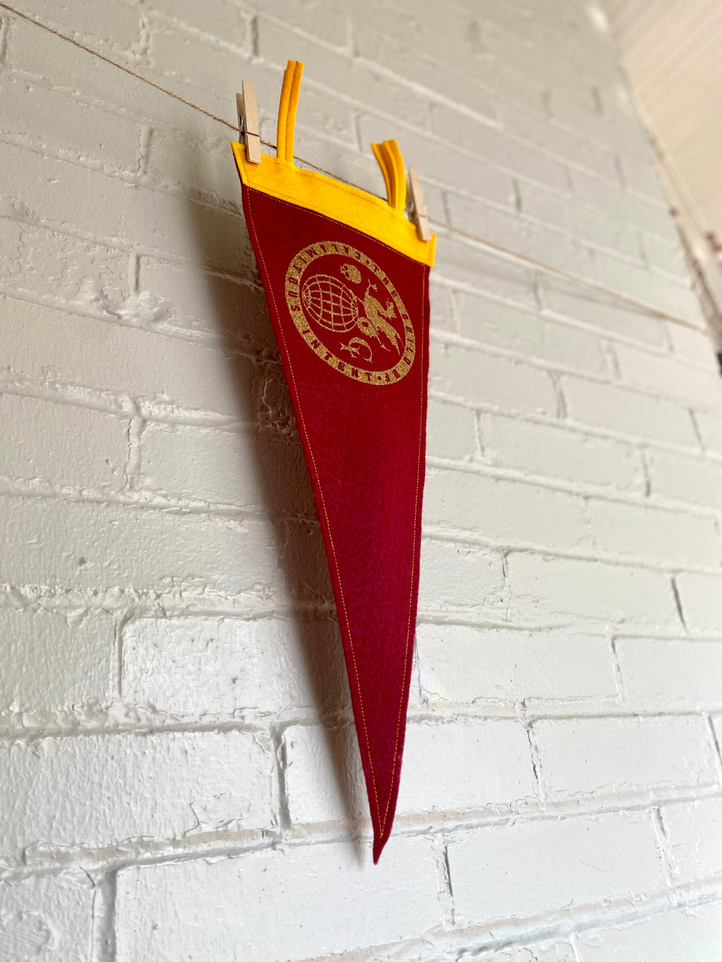 Side view of a burgundy pennant with yellow felt trim and the Guild of Calamitous Intent logo printed in gold
