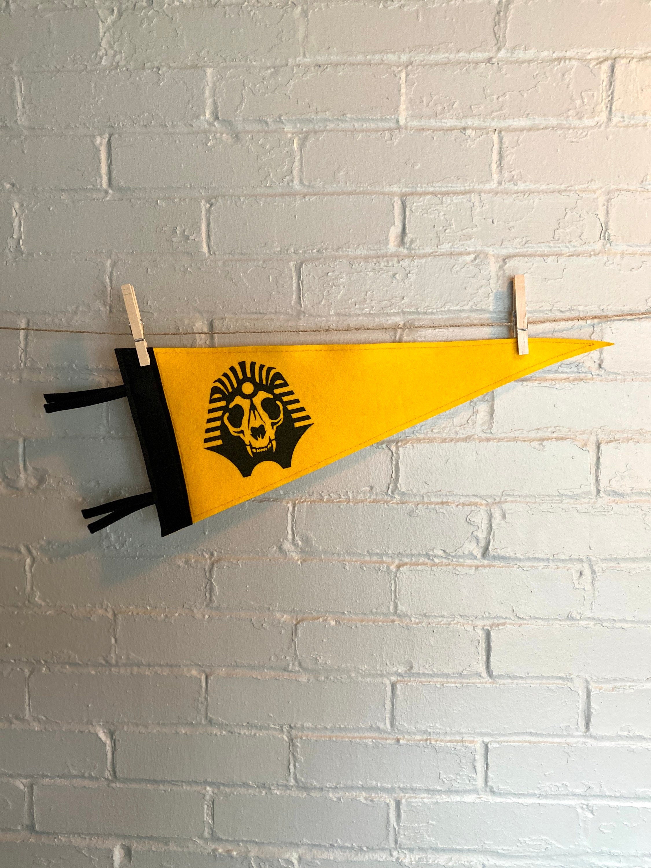 A yellow felt pennant with black trim and the SPHINX logo from The Venture Bros cartoon printed in black ink