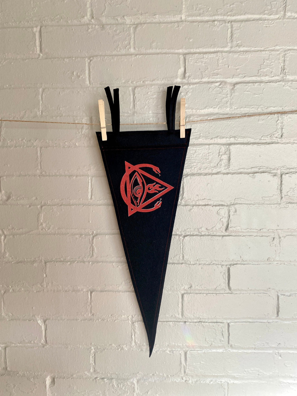 A black felt pennant with black trim and the Order of the Triad logo from The Venture Bros cartoon printed in red ink