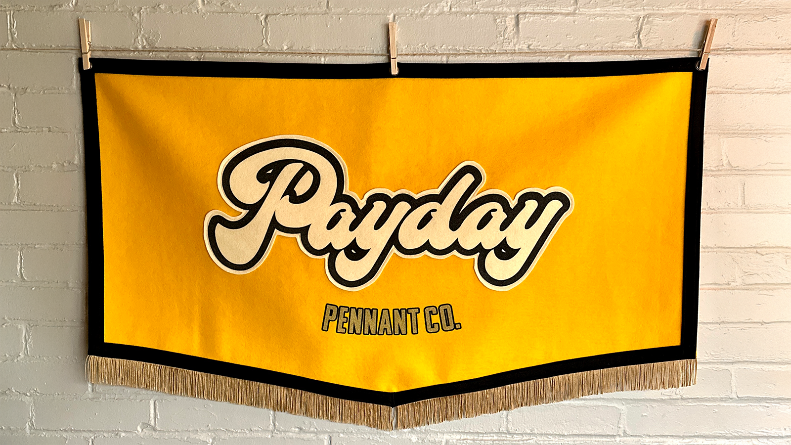 The Payday Pennant Co. logo on a large yellow and black felt banner with gold fringe